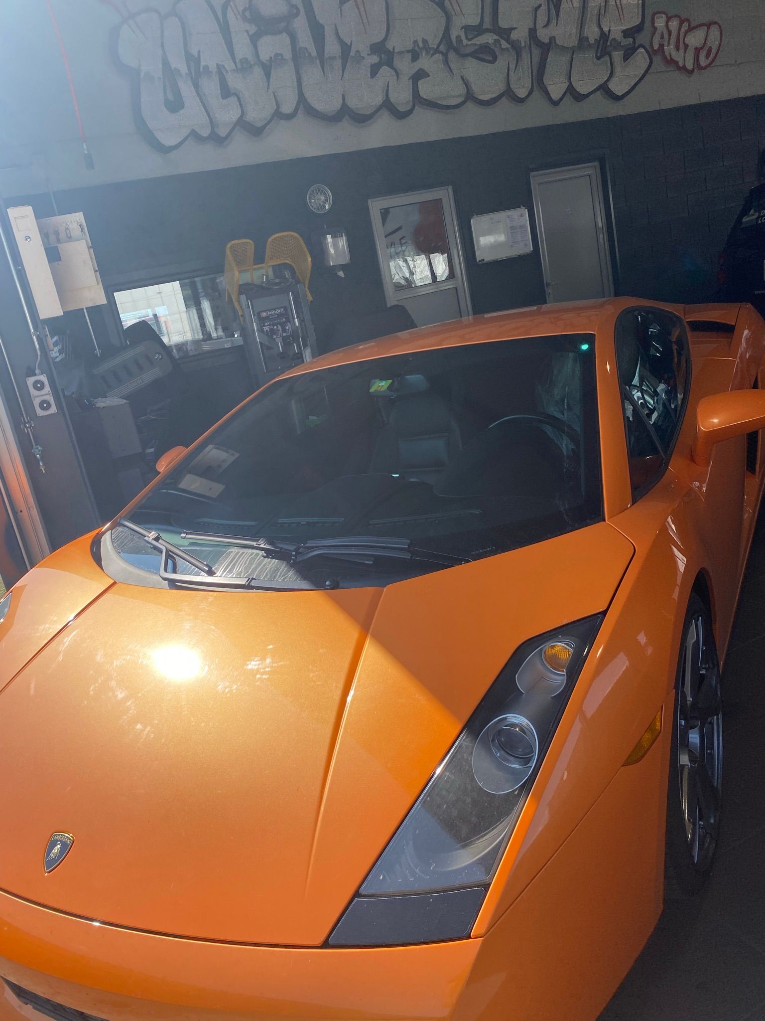 Une Lamborghini orange est garée devant un immeuble avec des graffitis dessus.