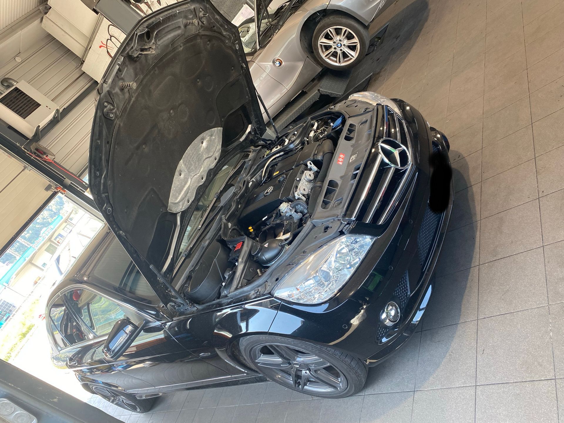 Une Mercedes noire avec le capot ouvert dans un garage