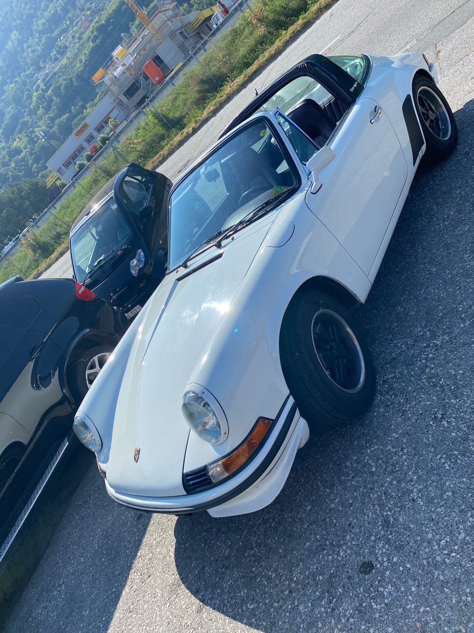 Une Porsche Targa blanche est garée sur le bord de la route à côté d’une voiture noire.