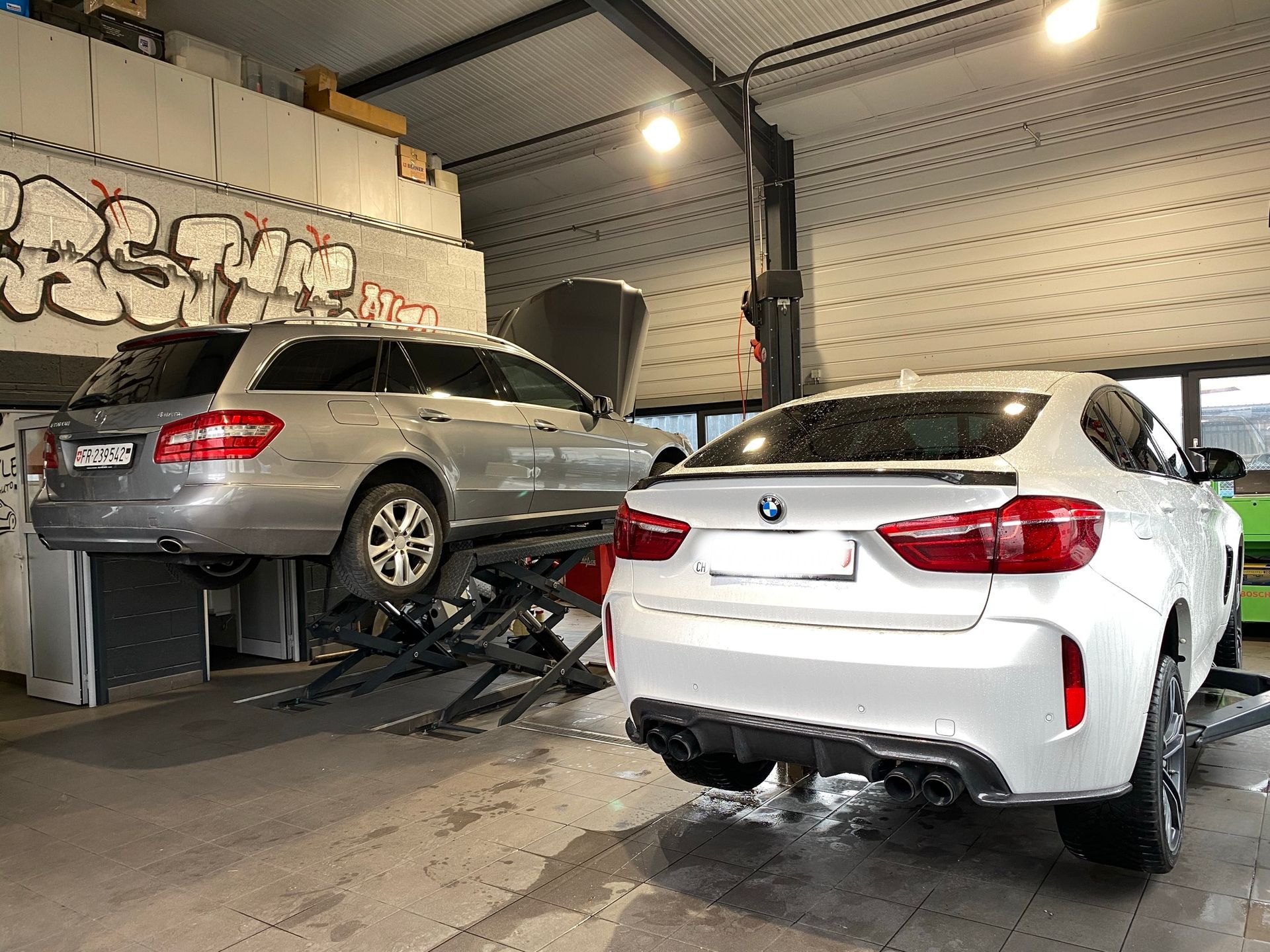 Deux voitures sont posées sur un ascenseur dans un garage.