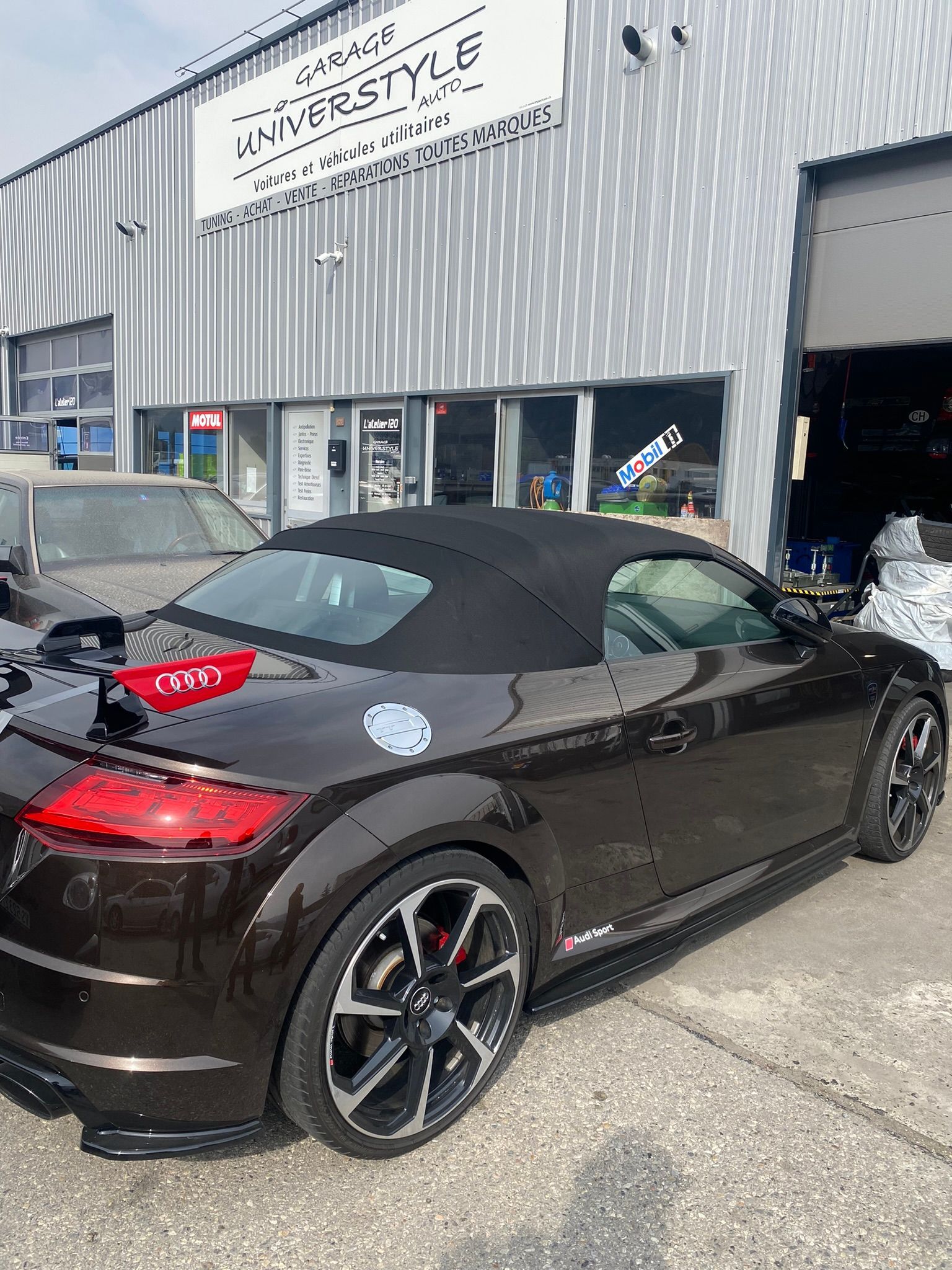 Une voiture de sport décapotable noire est garée devant un immeuble.