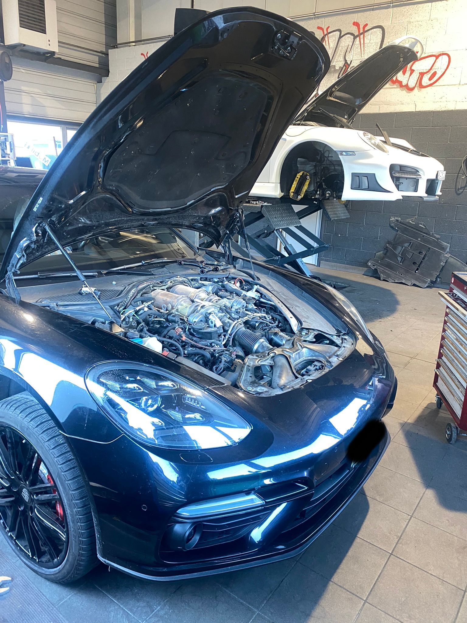 Une voiture noire avec le capot relevé dans un garage.