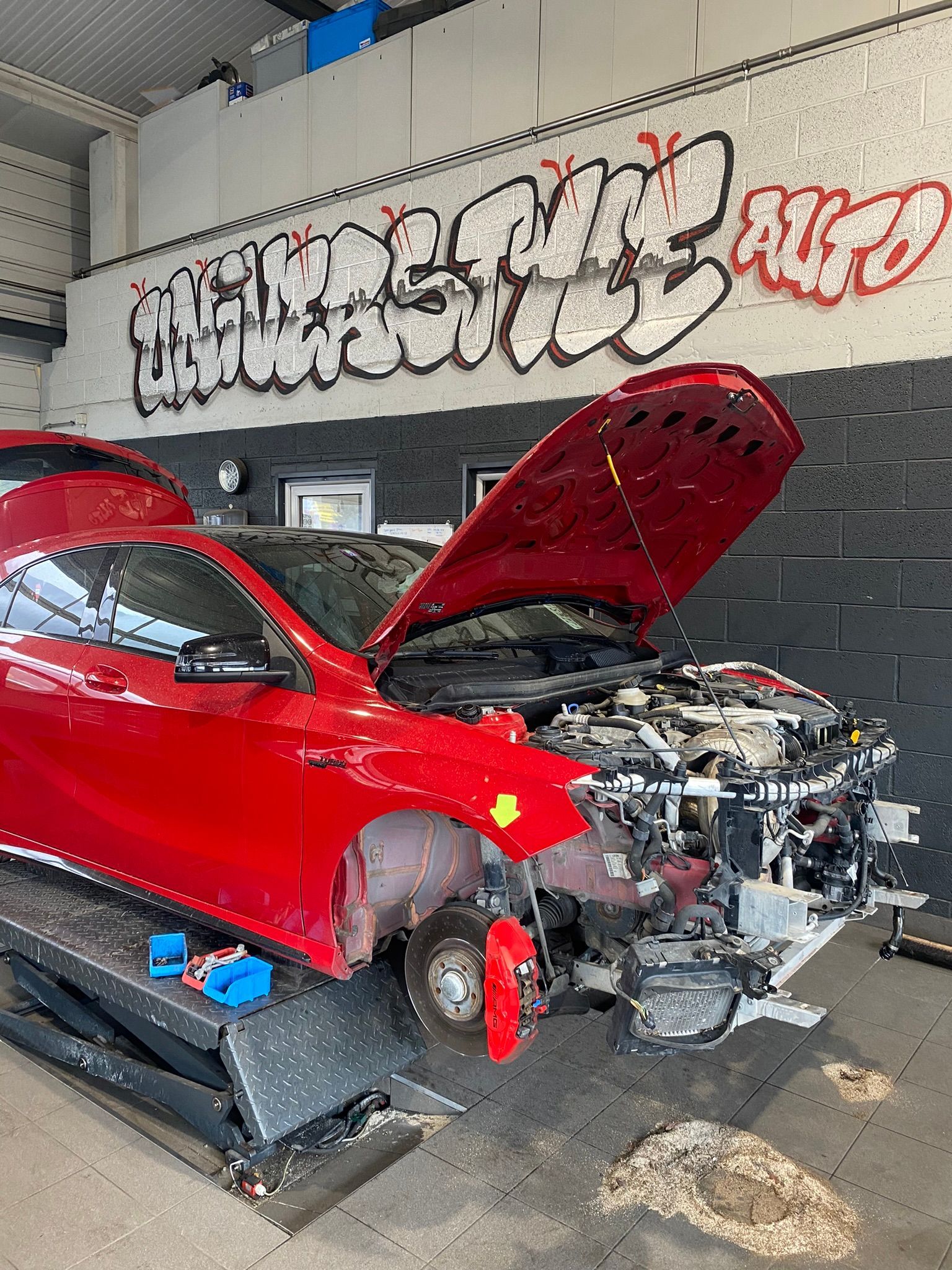 Une voiture rouge est assise sur un ascenseur dans un garage avec son capot ouvert.