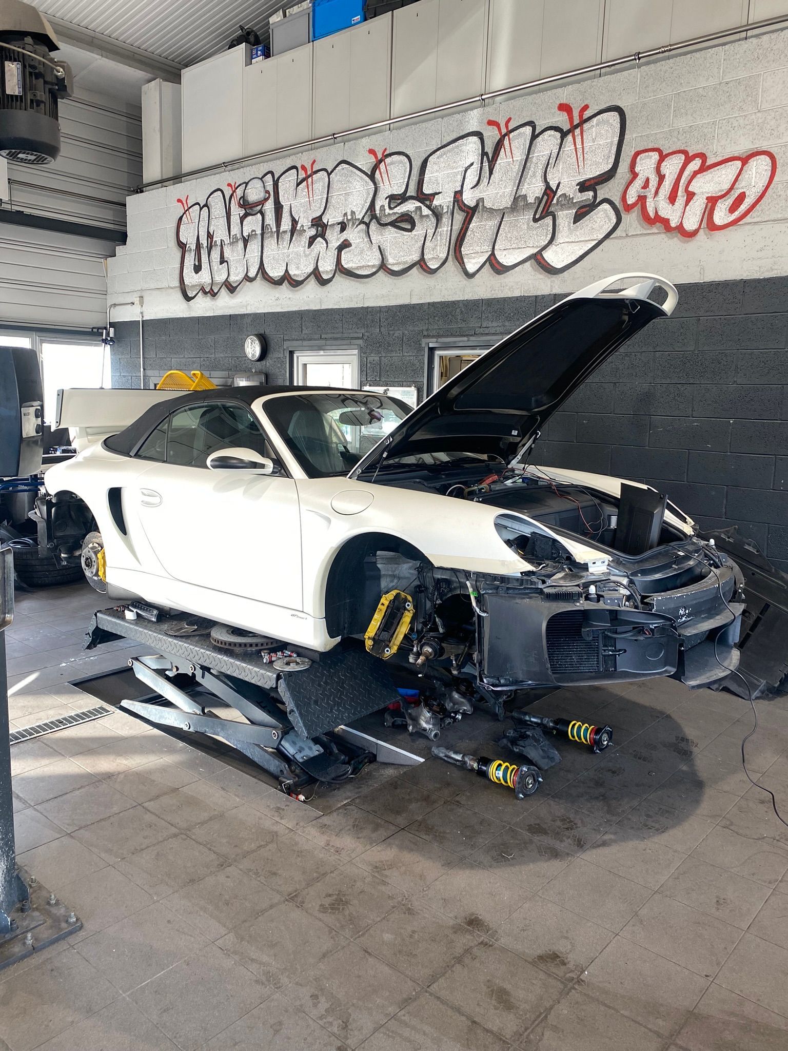 Une voiture de sport blanche avec le capot relevé est assise sur un ascenseur dans un garage.