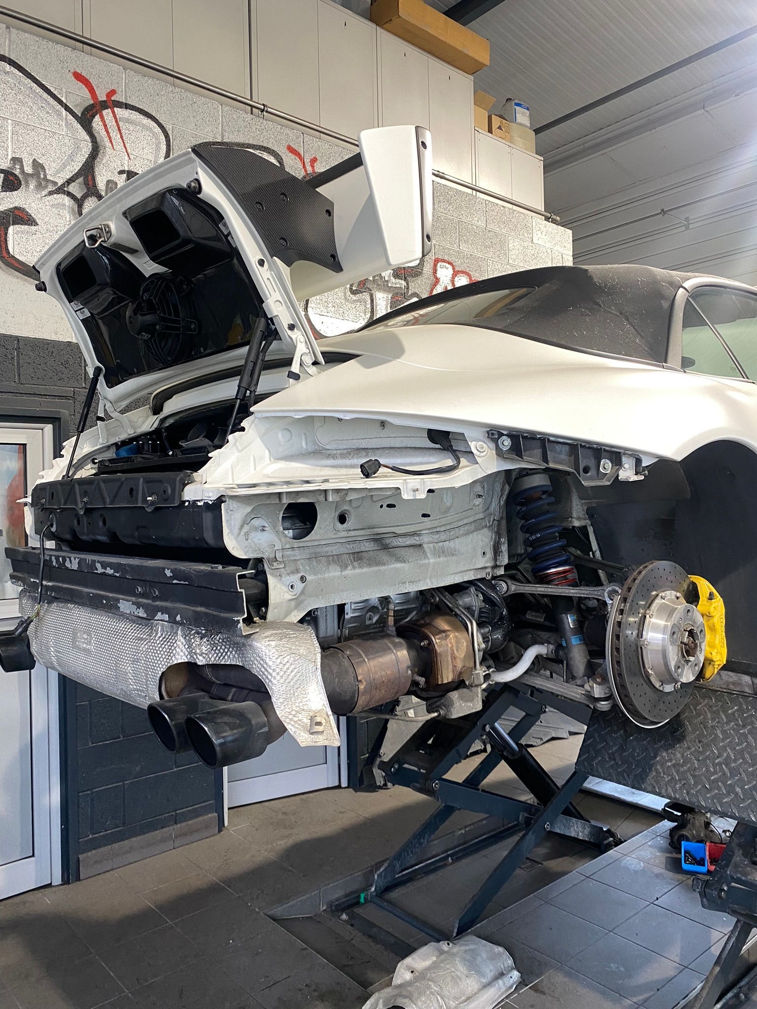 Une voiture blanche avec le capot ouvert est assise sur un ascenseur dans un garage.