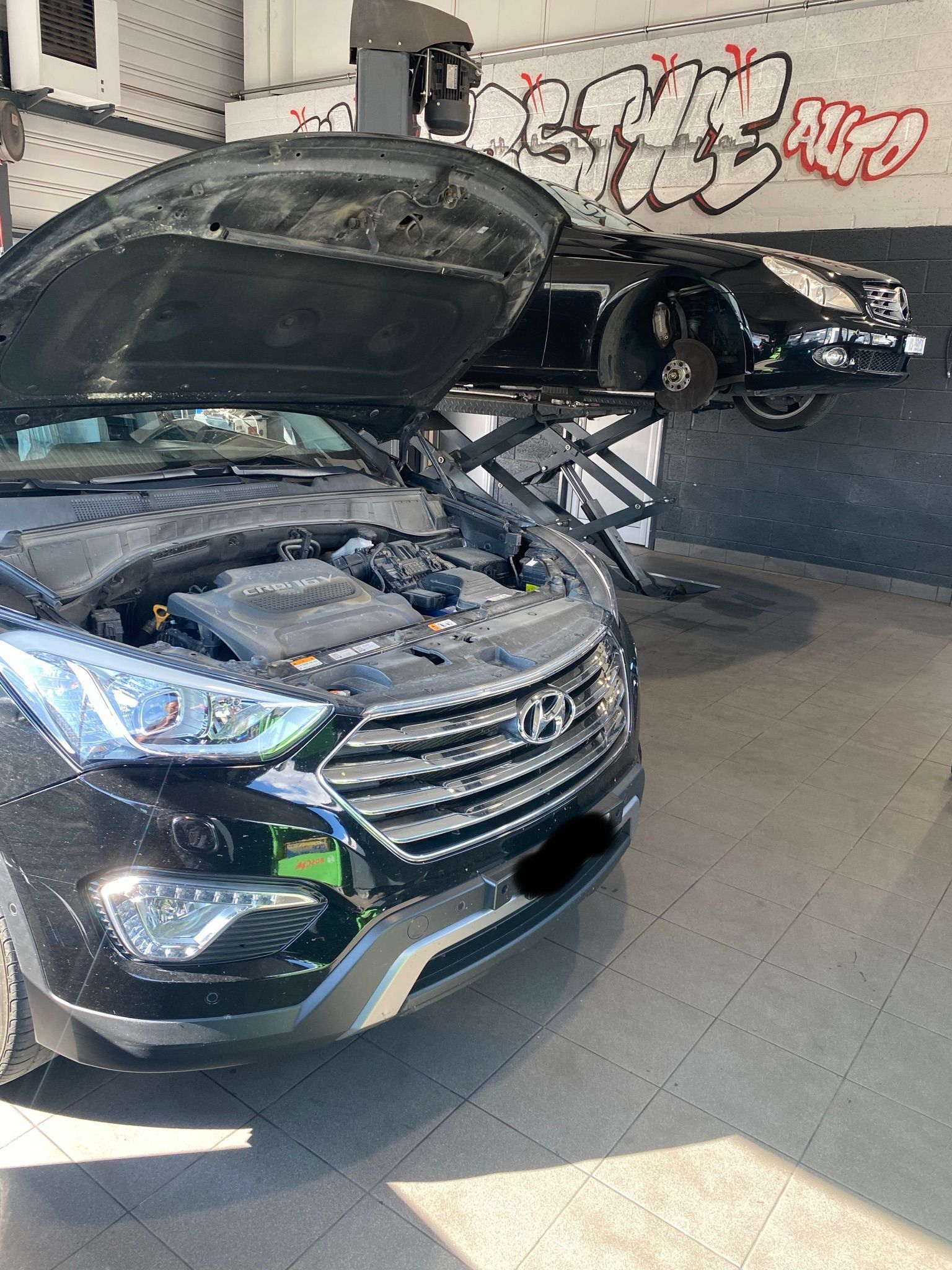 Une voiture noire avec le capot ouvert est garée dans un garage.