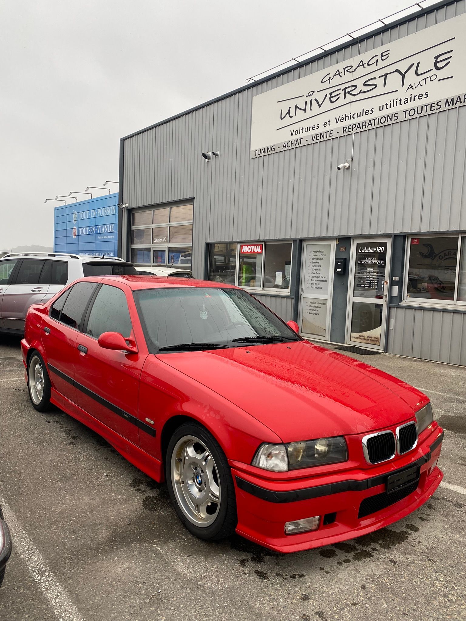 Une BMW rouge est garée devant un immeuble.