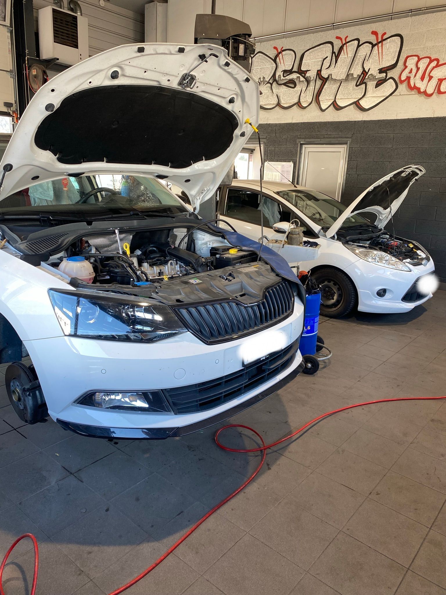 Une voiture blanche avec son capot ouvert dans un garage.