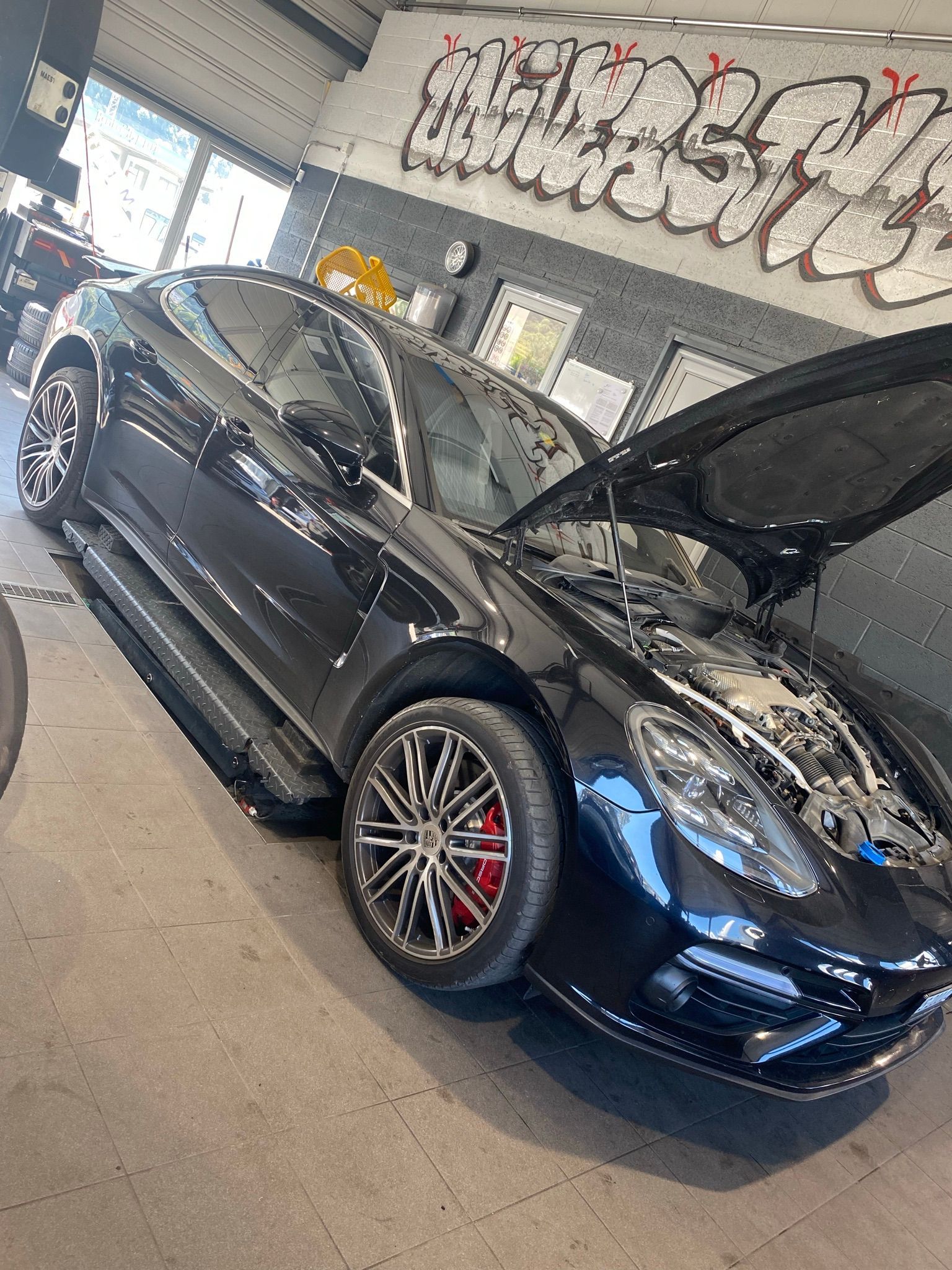 Une voiture noire avec le capot relevé est garée dans un garage.