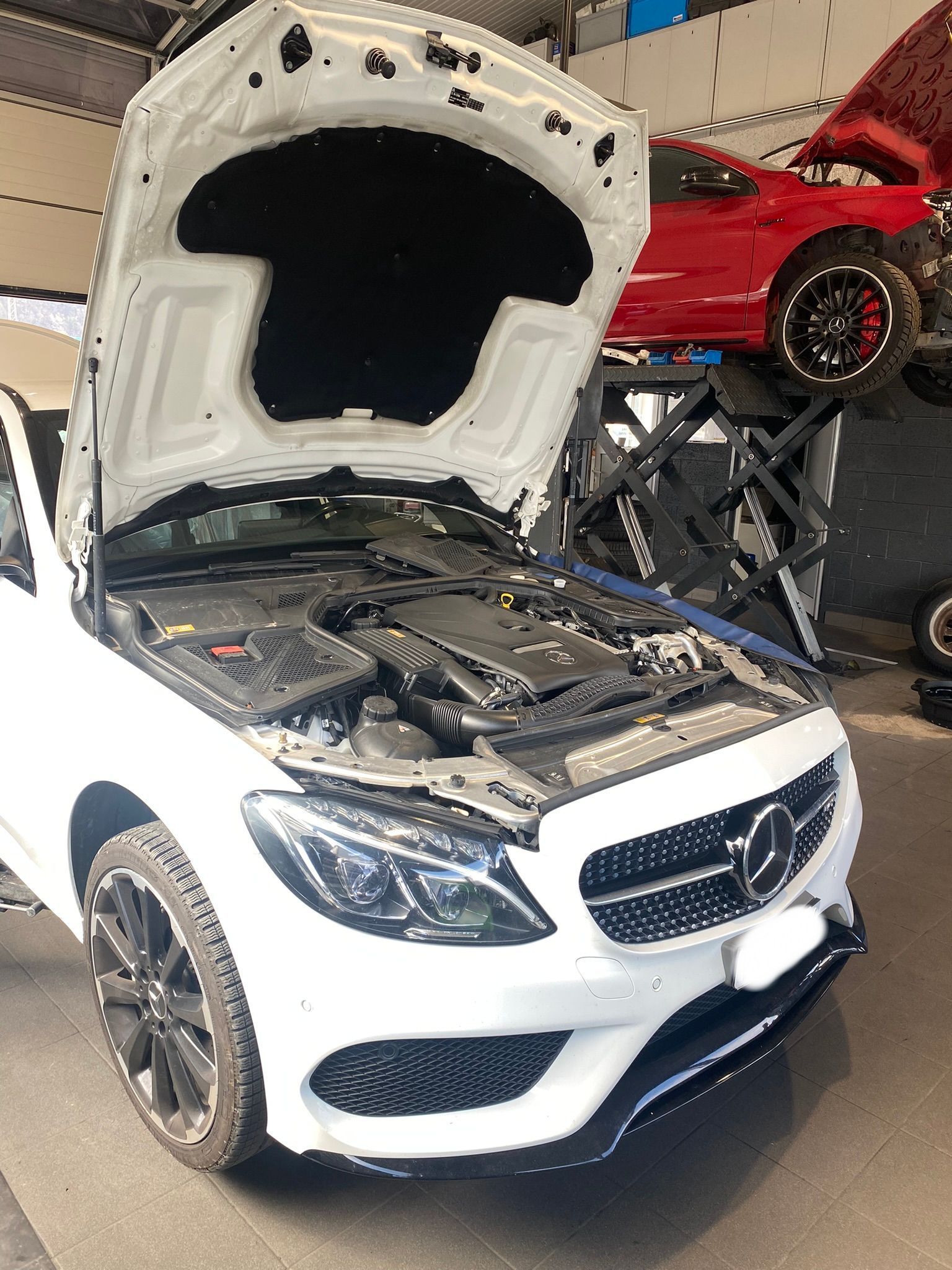 Une Mercedes Benz blanche avec le capot ouvert dans un garage.