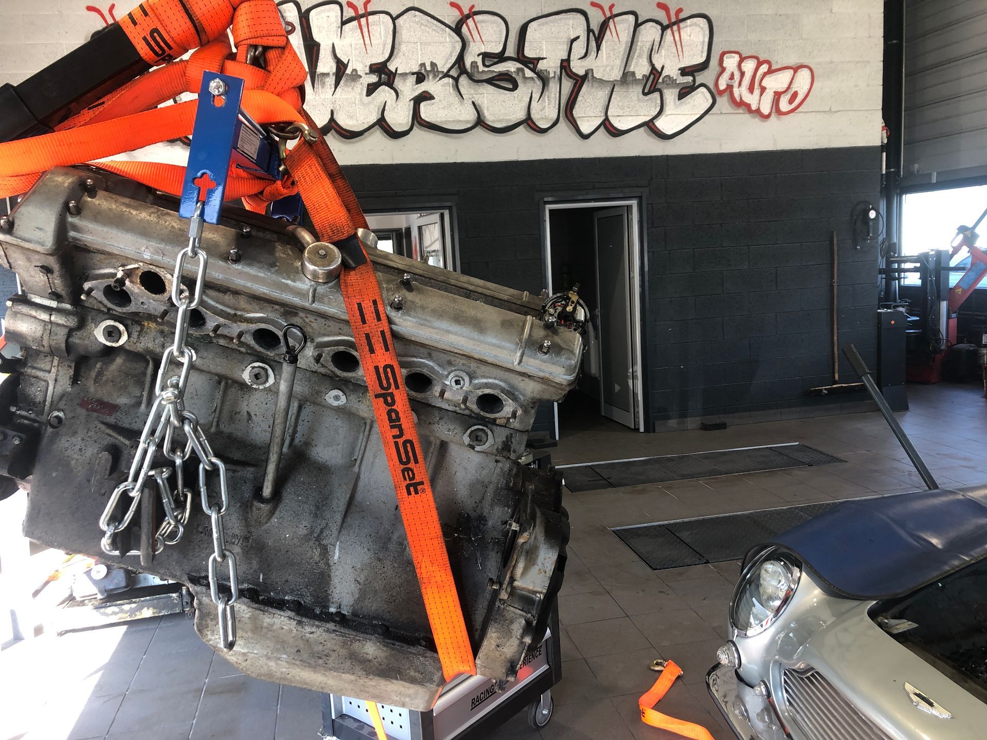 Un moteur de voiture est soulevé par une grue dans un garage.