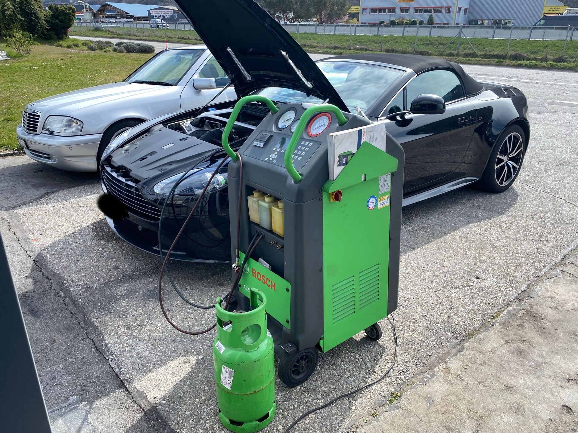 Une voiture avec son capot relevé est entretenue par une machine.