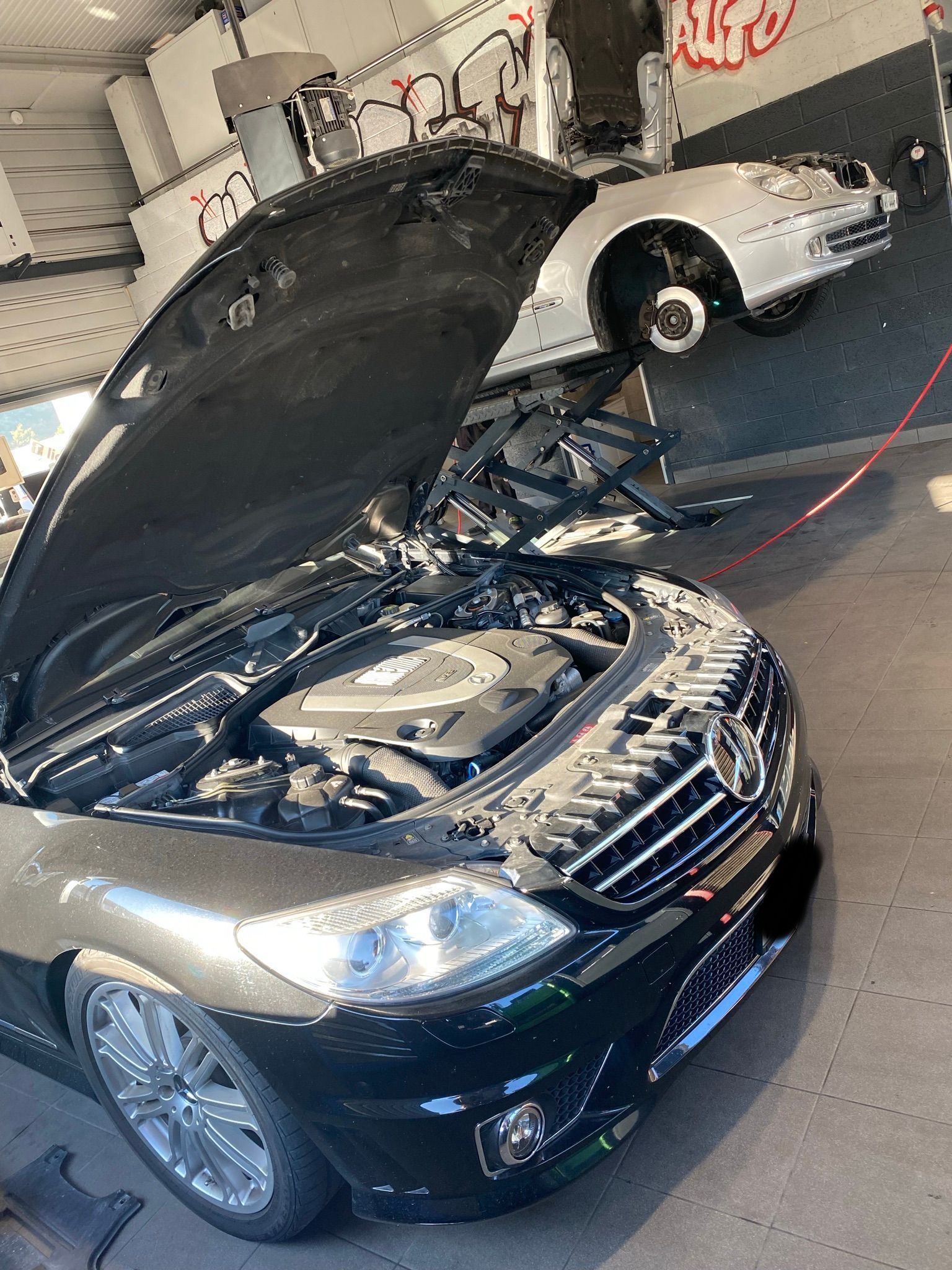 Une voiture noire avec le capot ouvert est garée dans un garage.