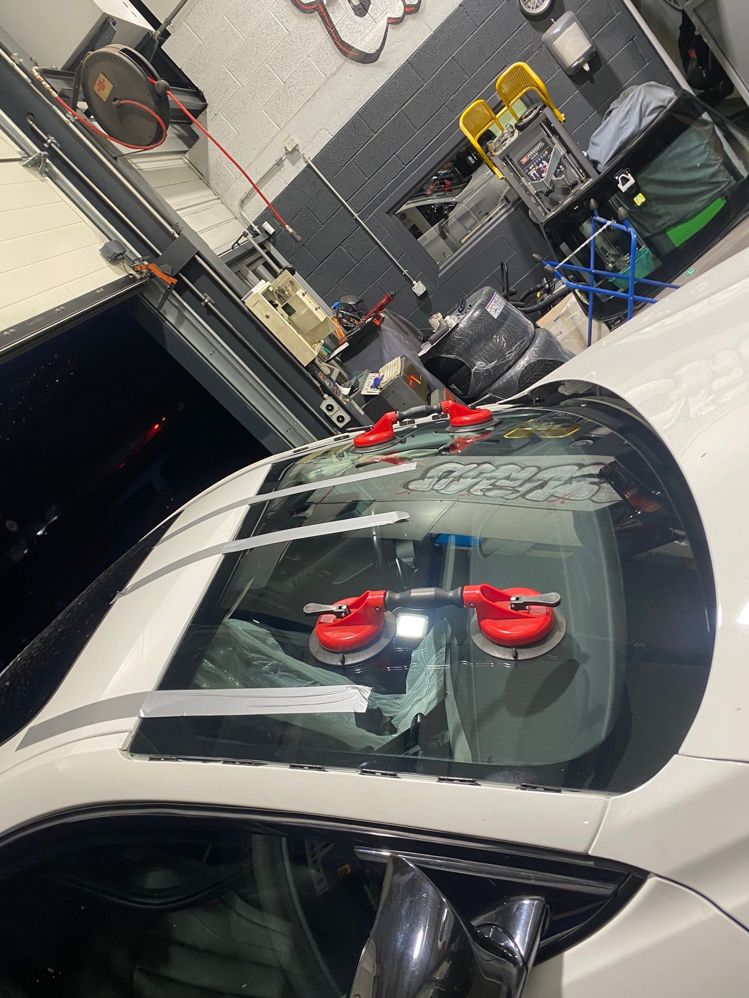 Une voiture blanche avec un pare-brise en cours de remplacement dans un garage.