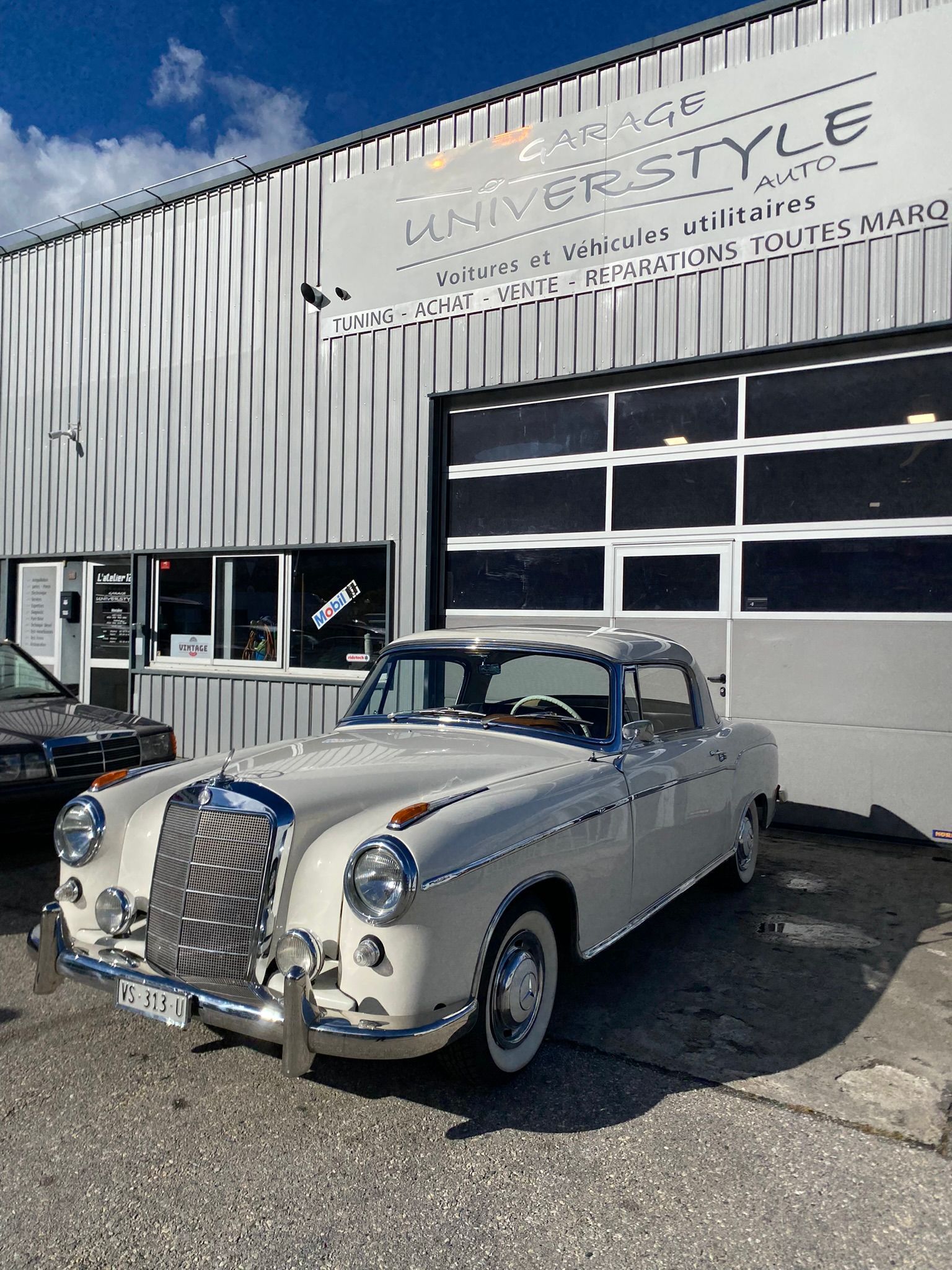 Une voiture blanche est garée devant un bâtiment qui dit style Mercedes