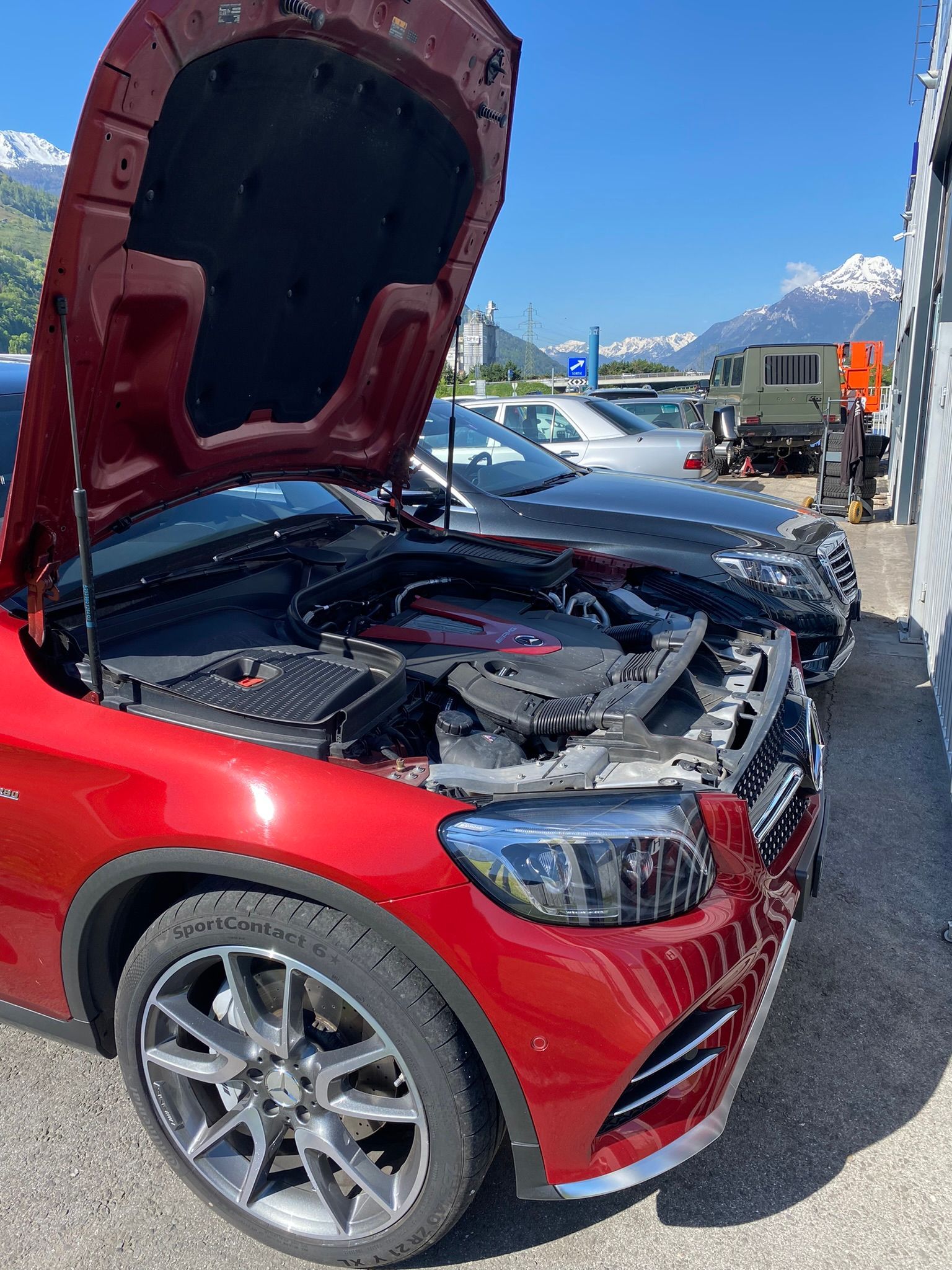 Une voiture rouge avec le capot relevé est garée dans un parking.