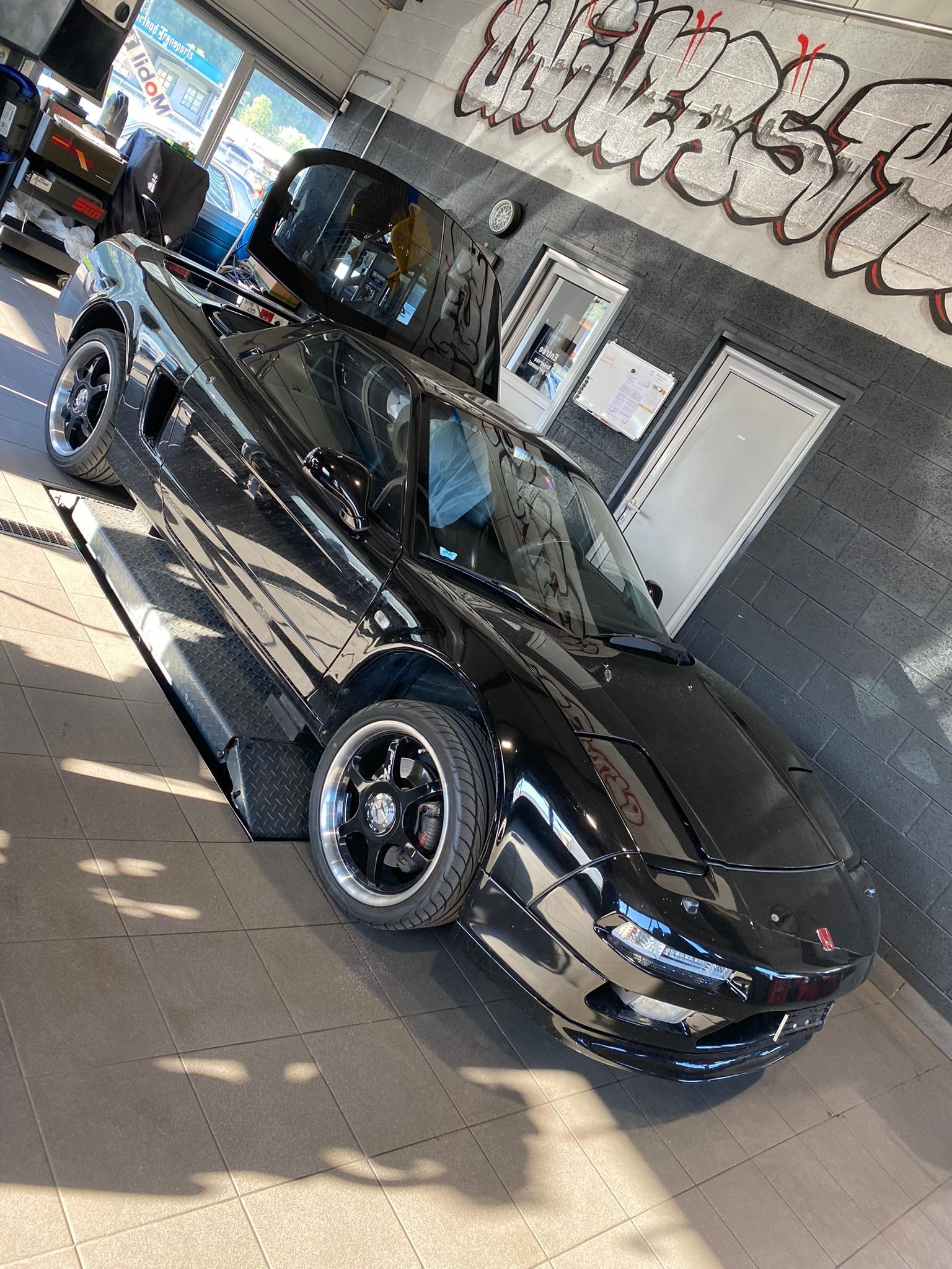 Une voiture noire est garée dans un garage avec des graffitis sur le mur.