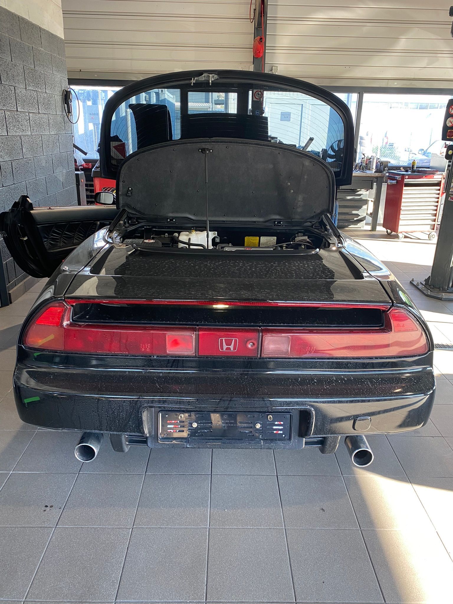 Une voiture de sport noire avec le capot relevé est garée dans un garage.