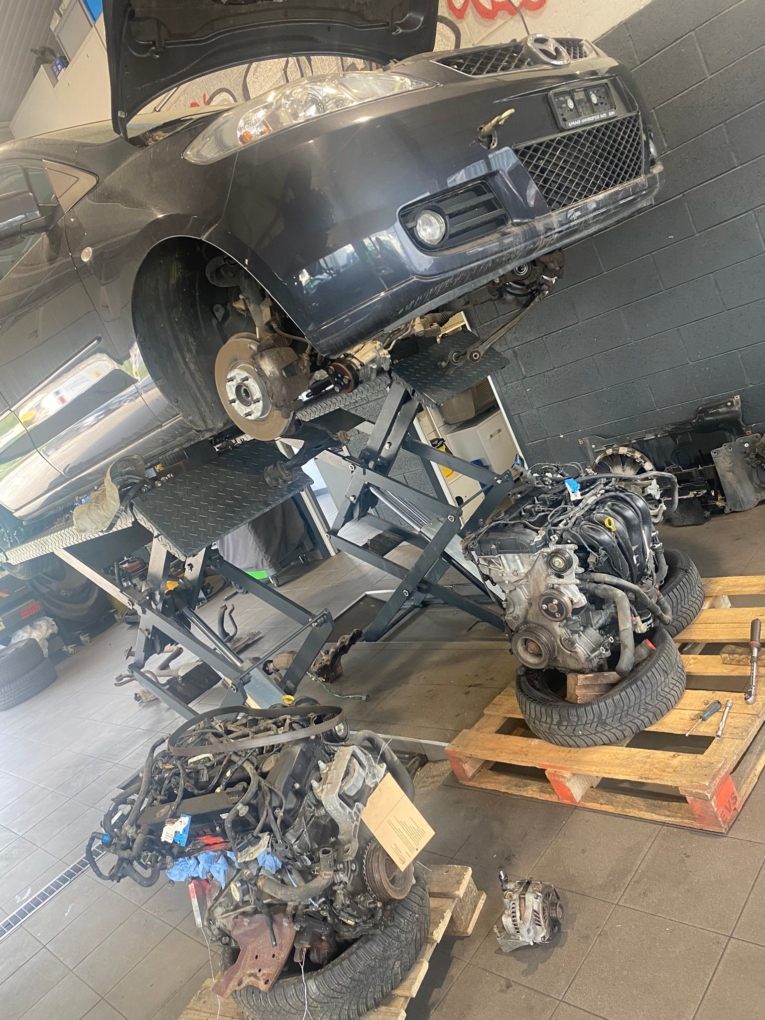 Une voiture est posée sur une palette en bois dans un garage.