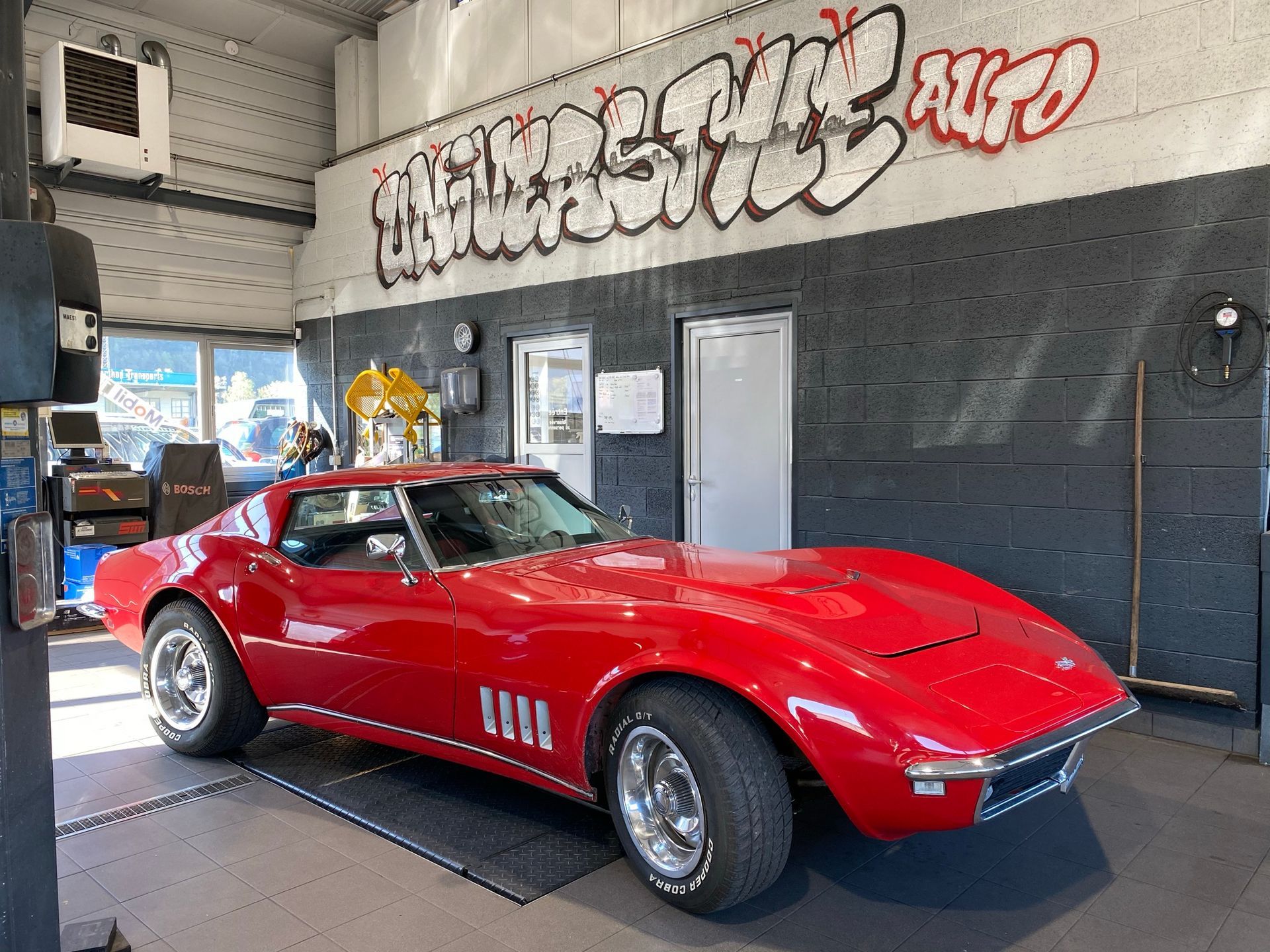 Une corvette rouge est garée dans un garage avec des graffitis sur le mur.