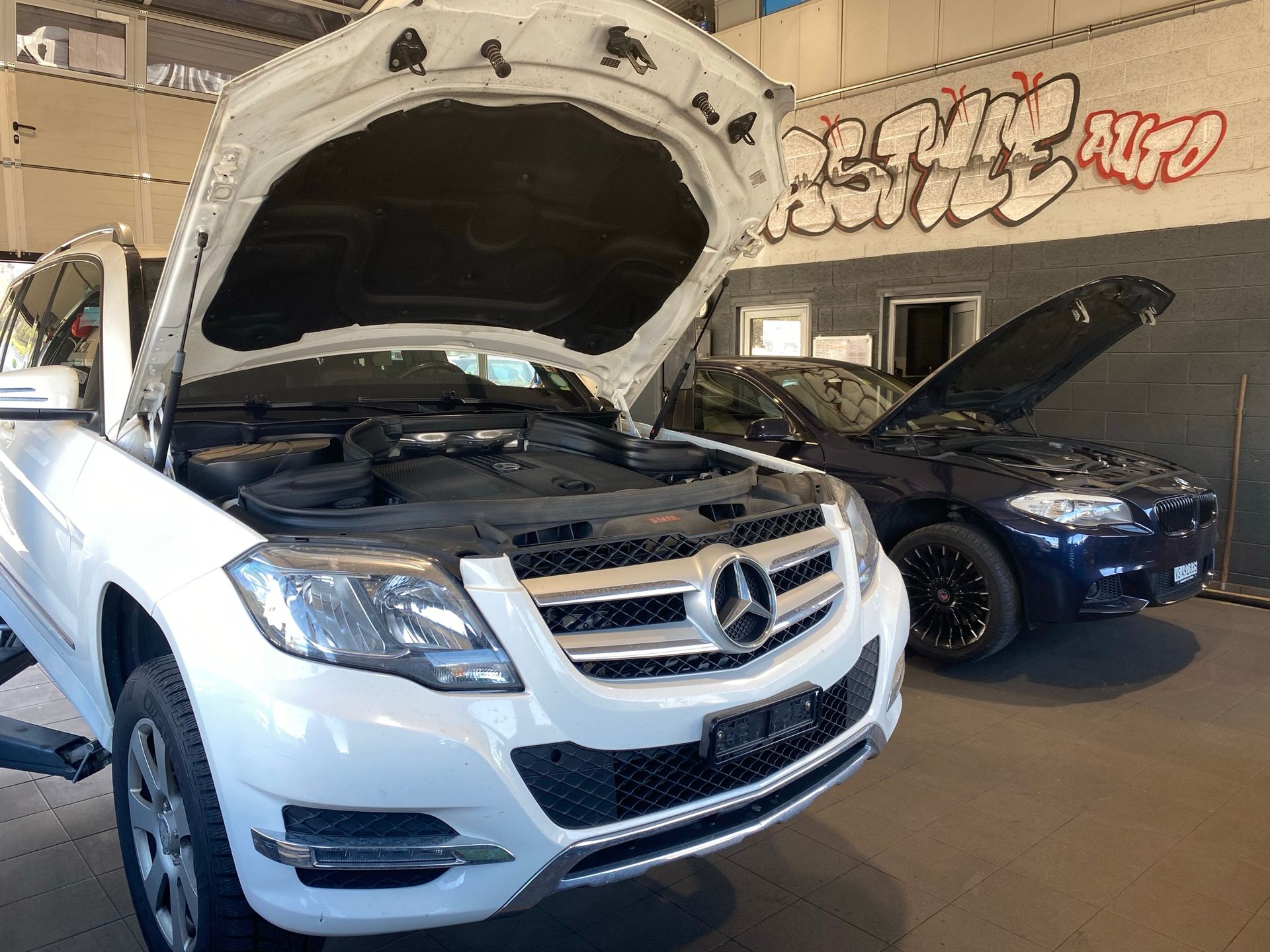 Une Mercedes Benz blanche avec le capot ouvert est garée dans un garage.