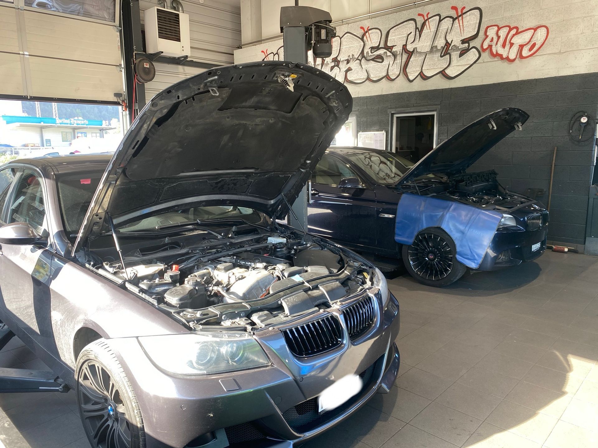 Deux voitures sont garées dans un garage avec le capot ouvert.