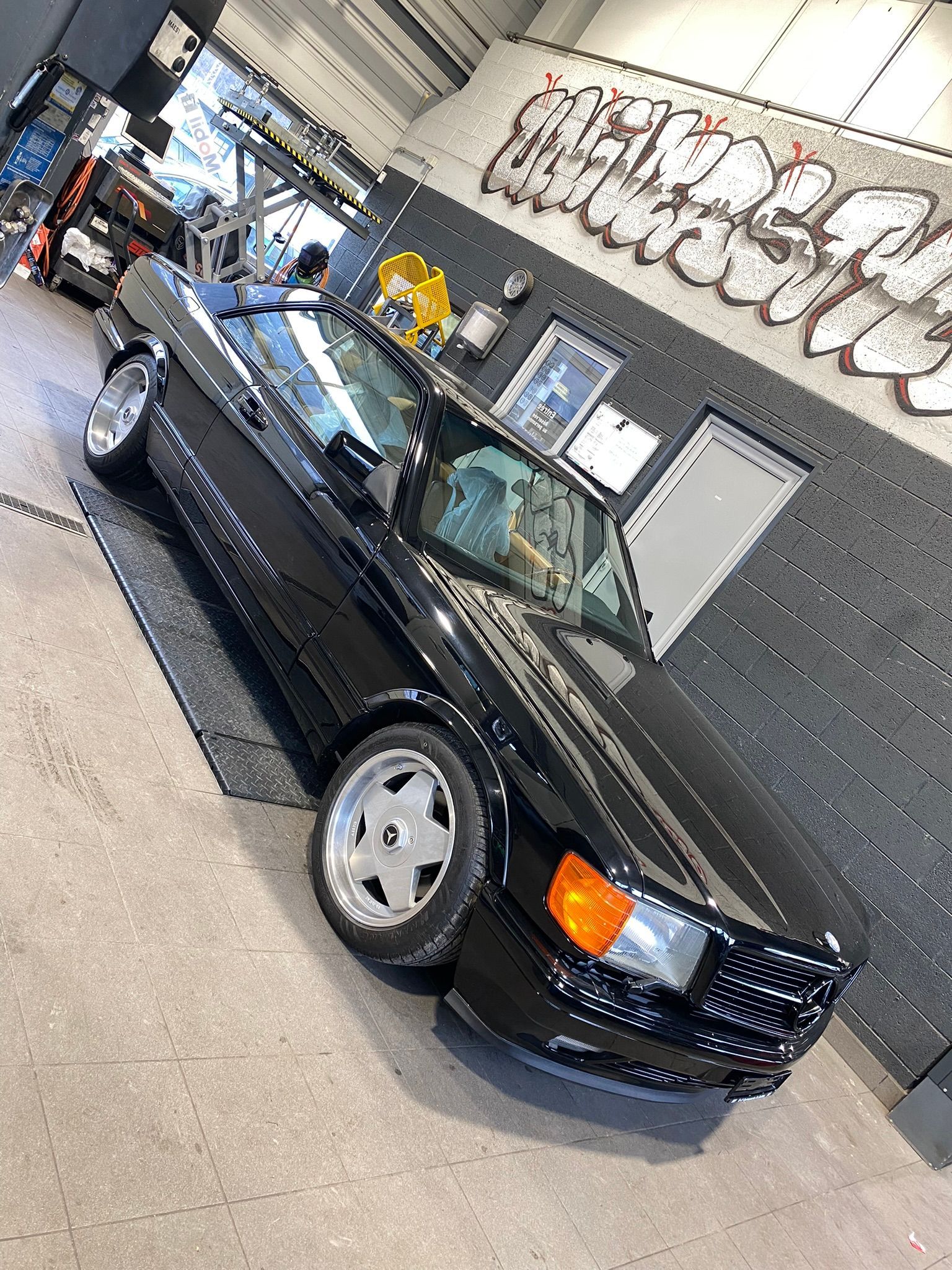 Une voiture noire est garée devant un mur avec des graffitis dessus.