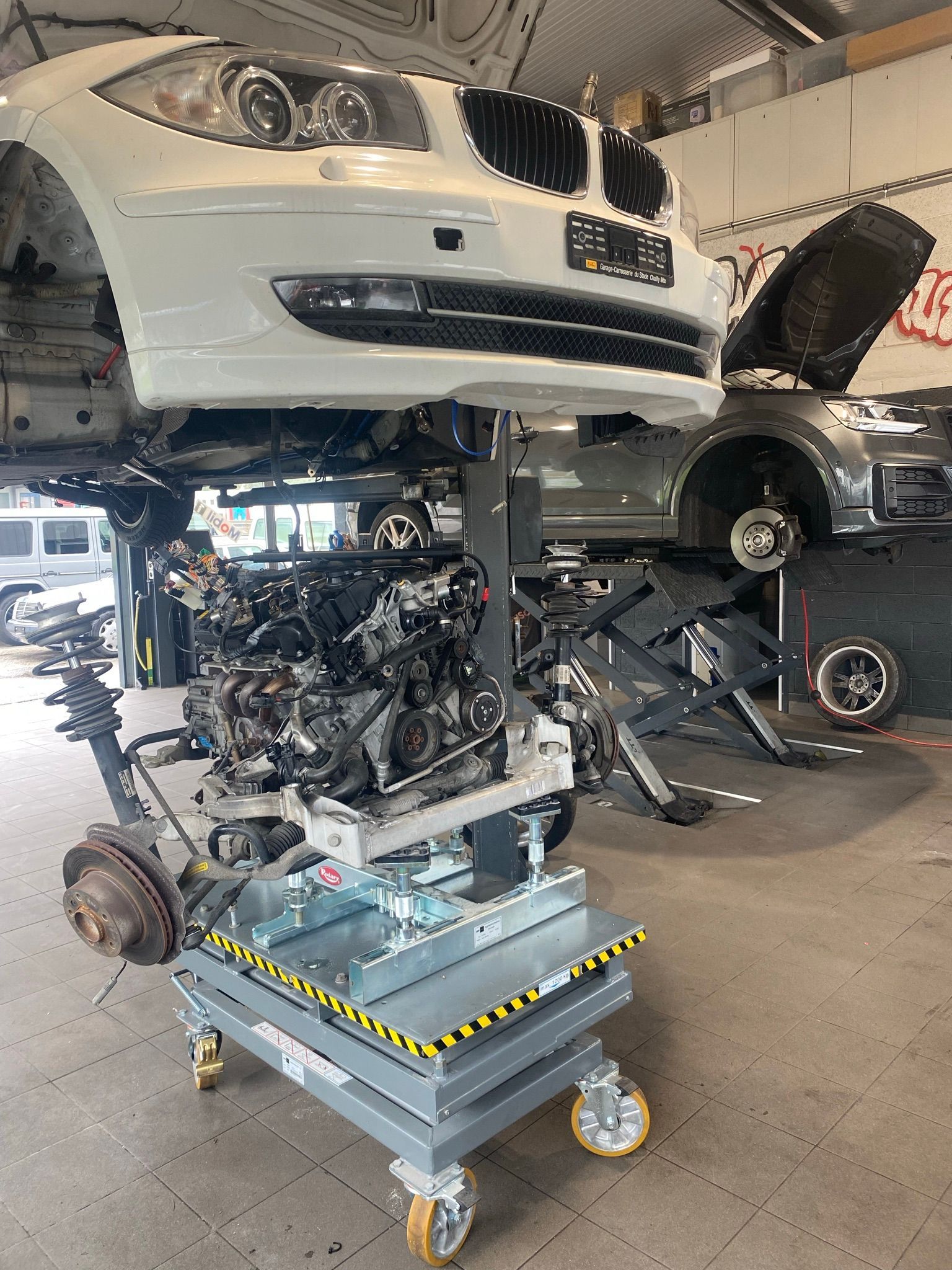 Une BMW blanche est en train d'être démontée dans un garage.