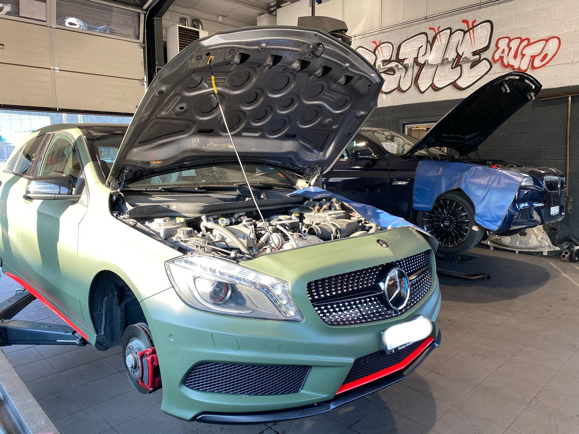 Une Mercedes Benz verte avec son capot ouvert dans un garage.