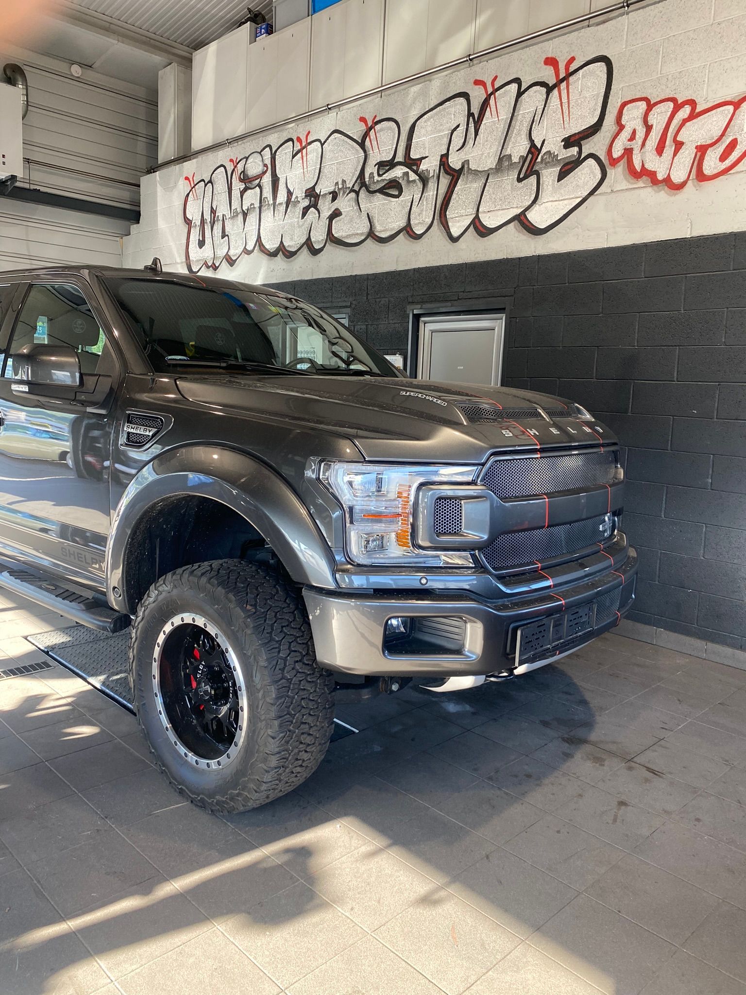 Un Ford F150 Raptor est garé devant un mur avec des graffitis dessus.