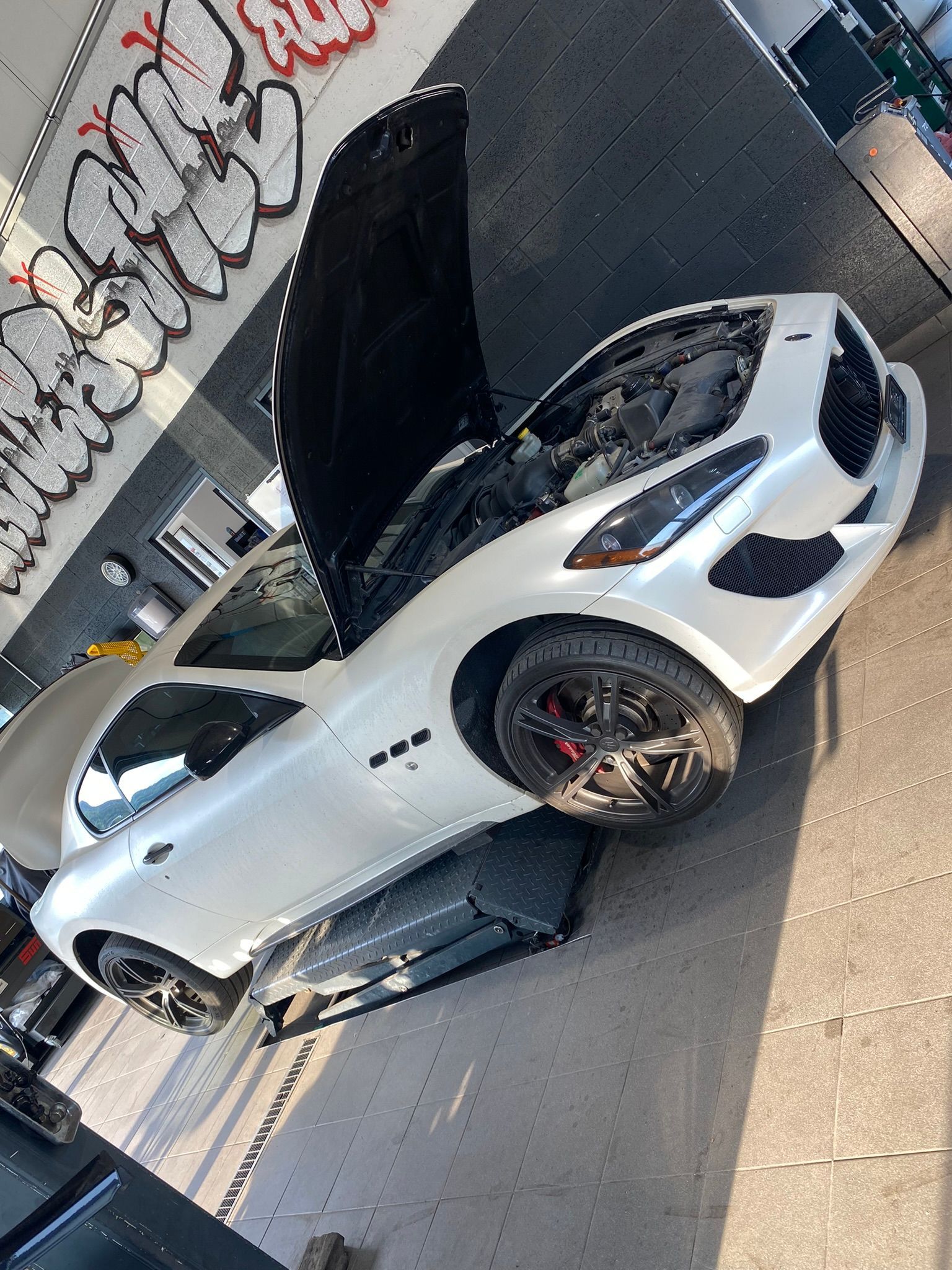 Une voiture de sport blanche avec le capot relevé est assise sur un ascenseur.
