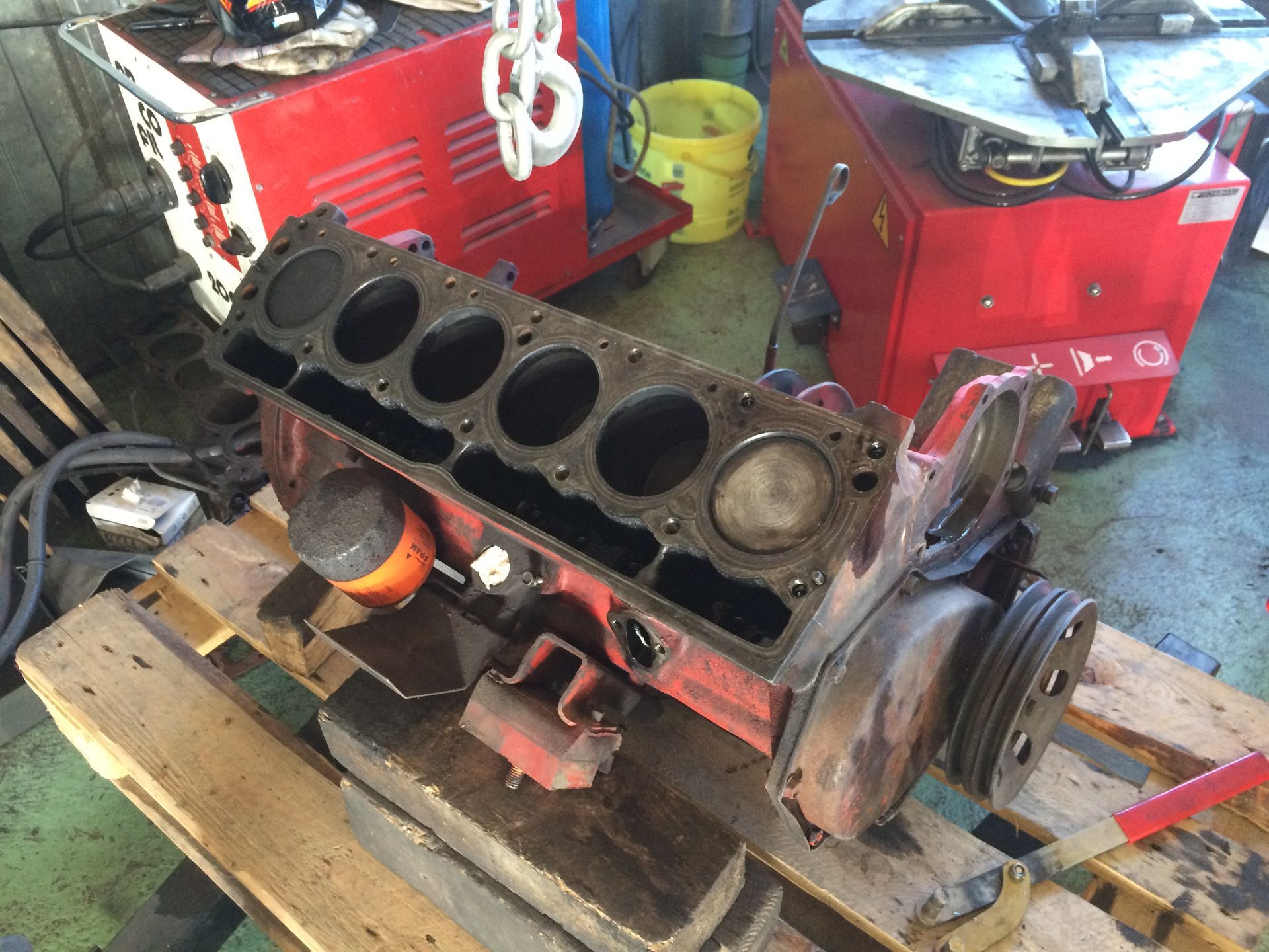 Un bloc moteur rouge est posé sur une palette en bois dans un garage.