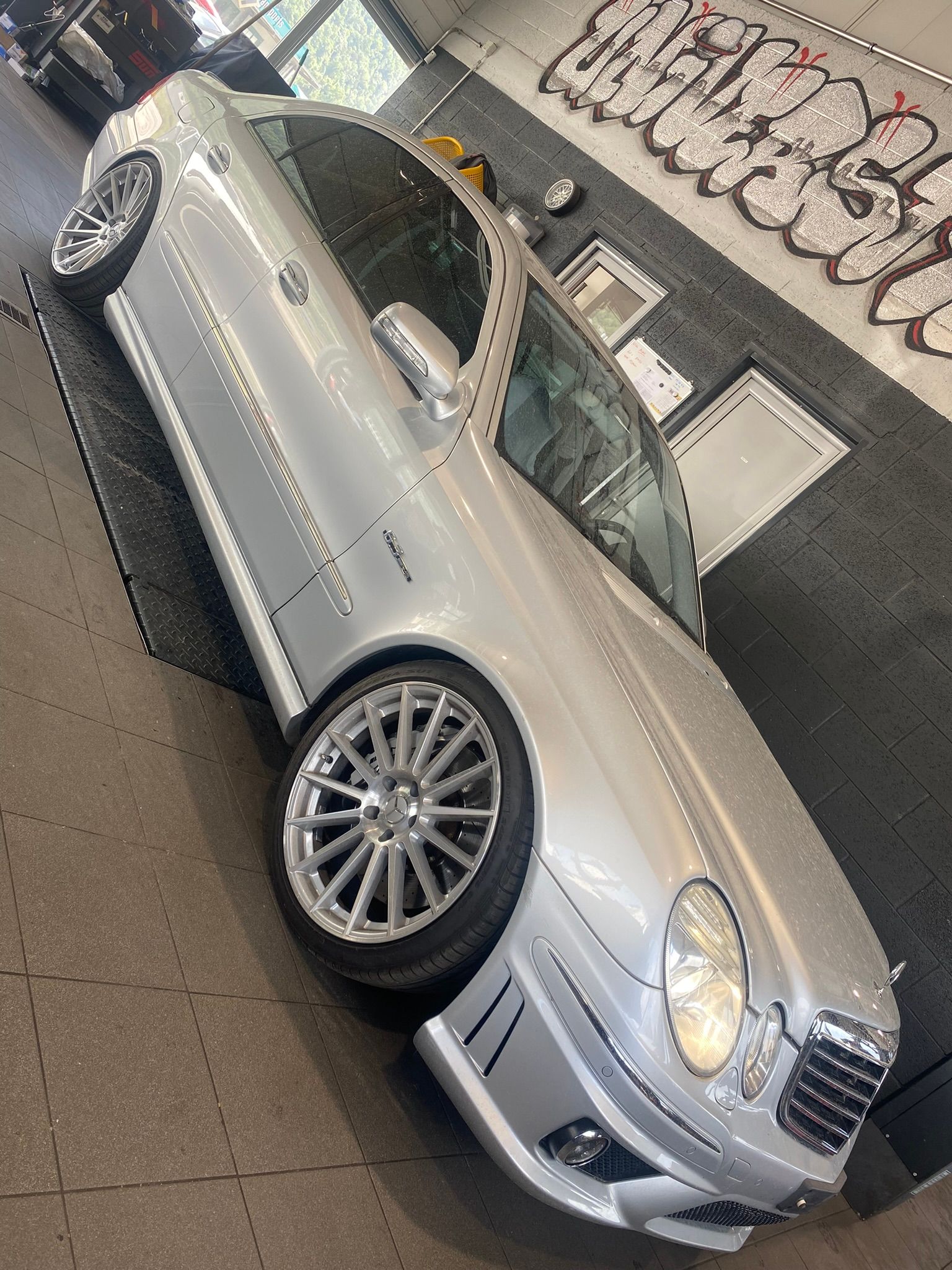 Une voiture argentée est garée dans un garage avec des graffitis sur le mur.