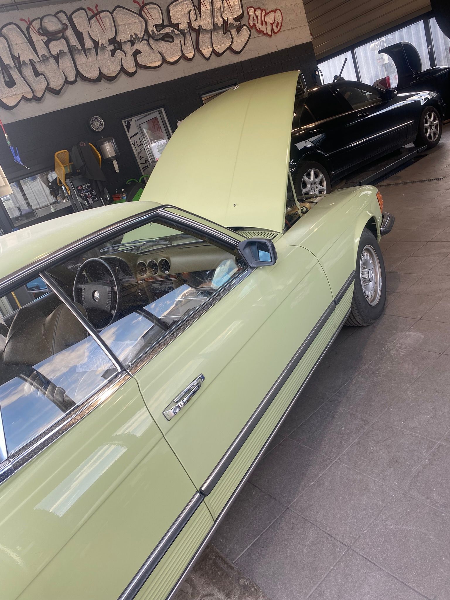 Une voiture verte avec le capot relevé est garée dans un garage.