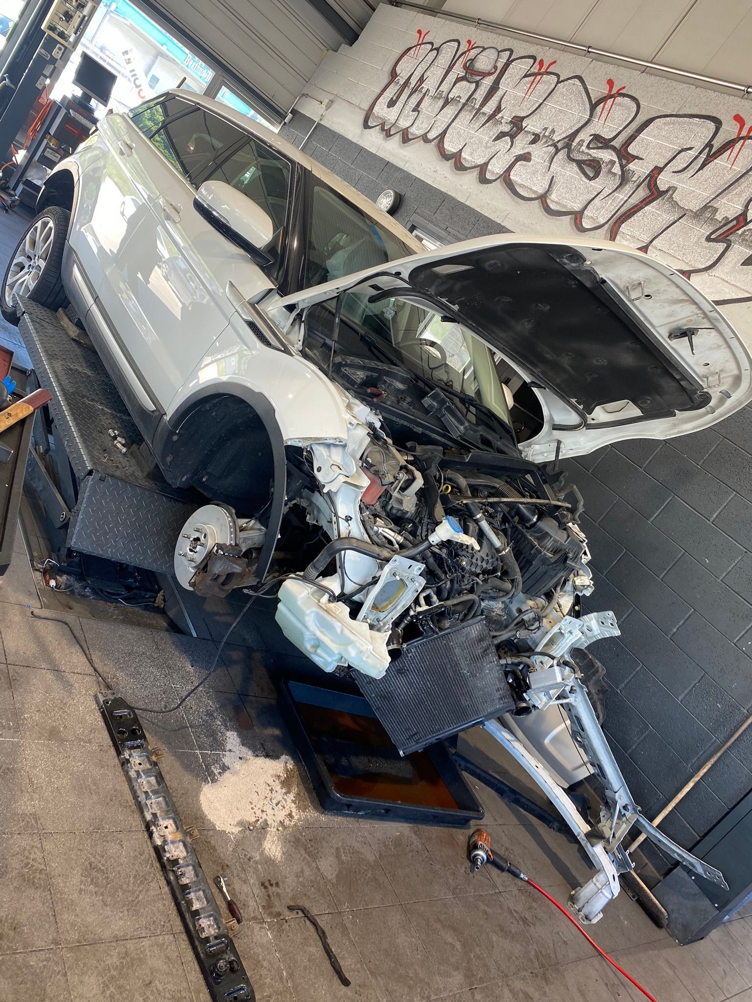 Une voiture blanche est assise sur un ascenseur dans un garage avec son capot ouvert.