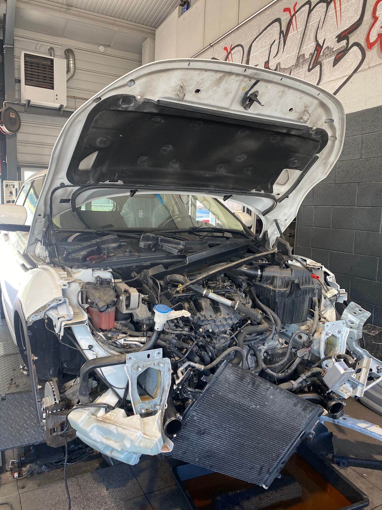 Une voiture blanche avec le capot ouvert est assise dans un garage.