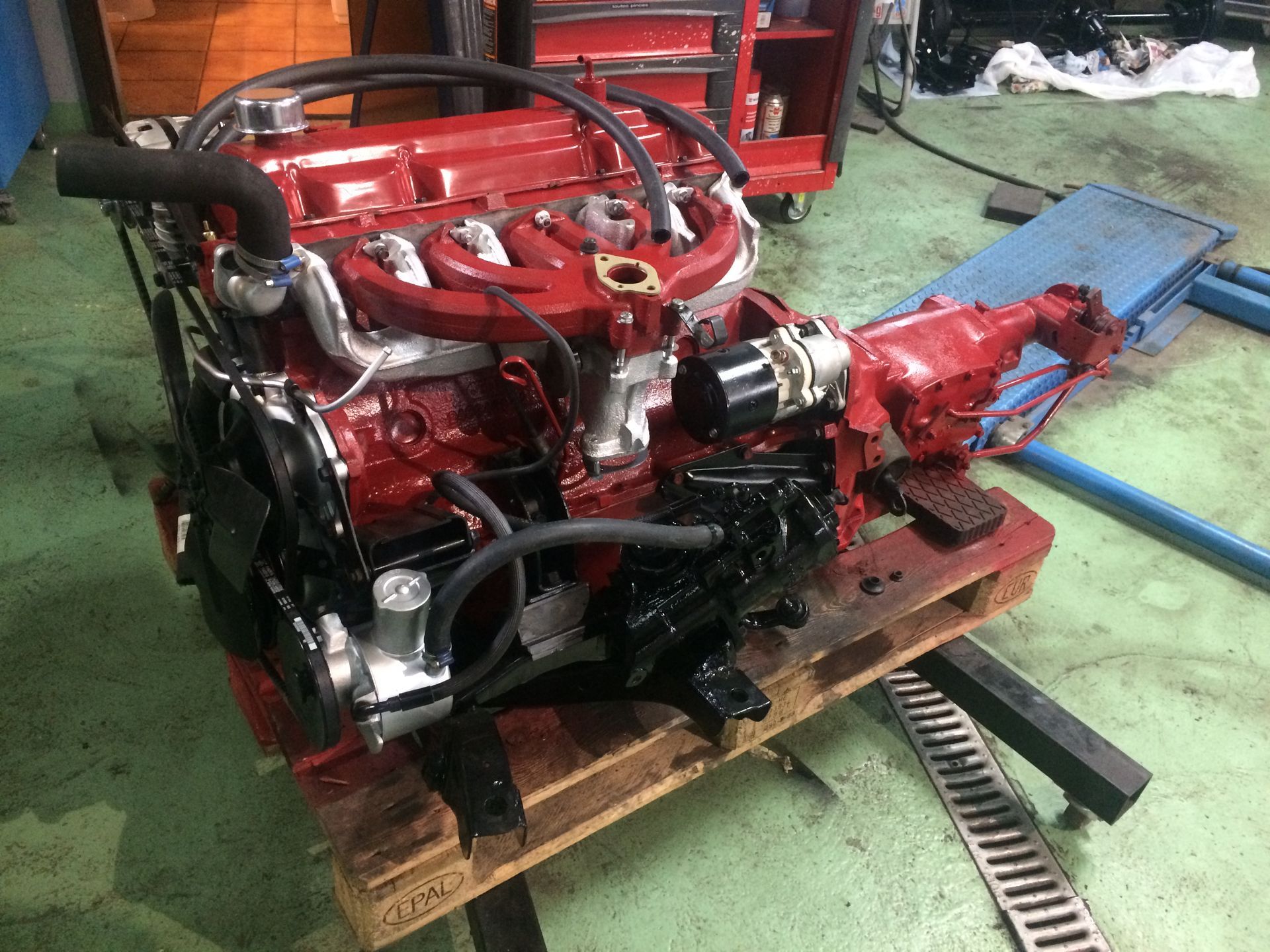 Un moteur rouge est posé sur une palette en bois dans un garage.