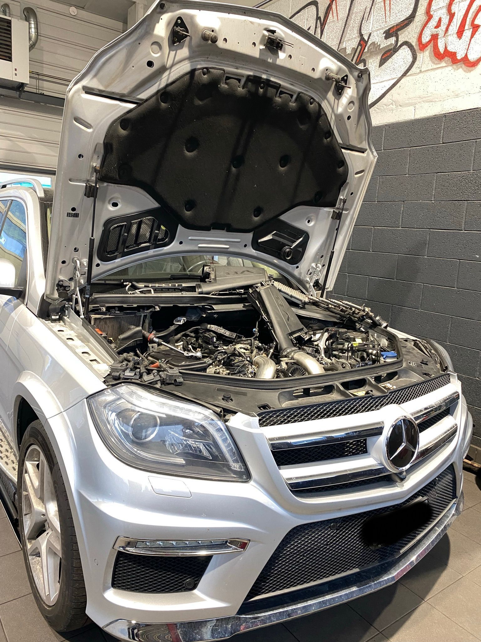 Une Mercedes Benz argentée avec le capot ouvert est garée sur le bord de la route.