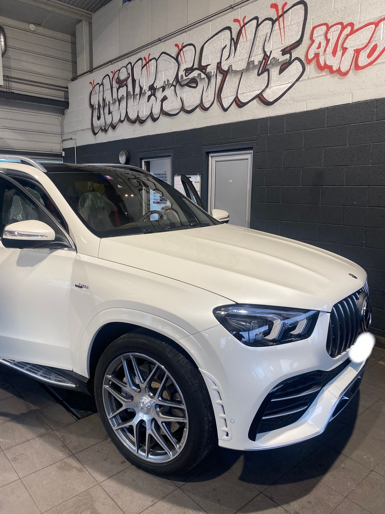 Un SUV blanc est garé devant un mur avec des graffitis dessus.