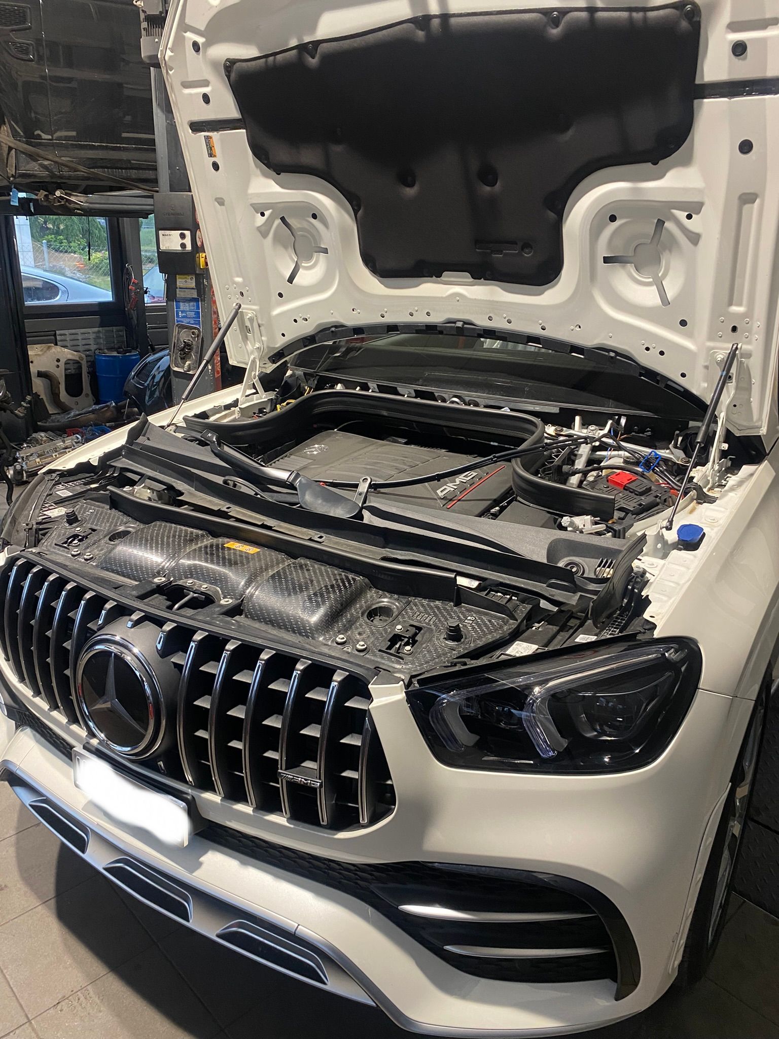 Une Mercedes Benz blanche avec le capot ouvert dans un garage.