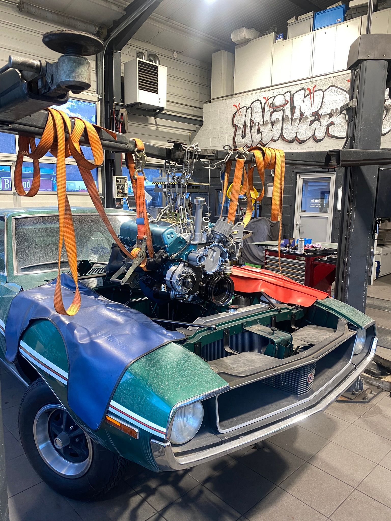 Une voiture verte est soulevée par une grue dans un garage.