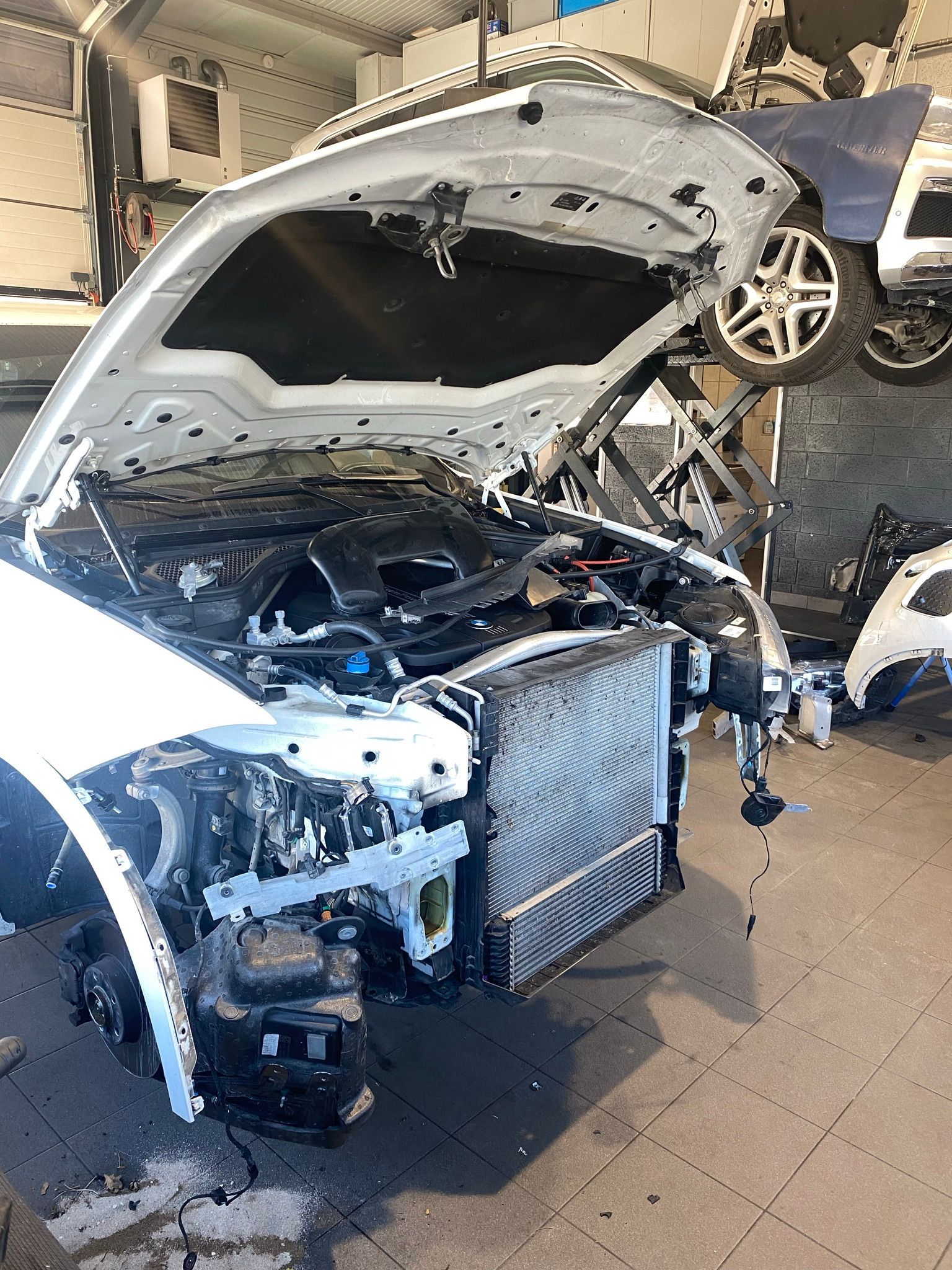 Une voiture blanche est démontée dans un garage avec le capot ouvert.