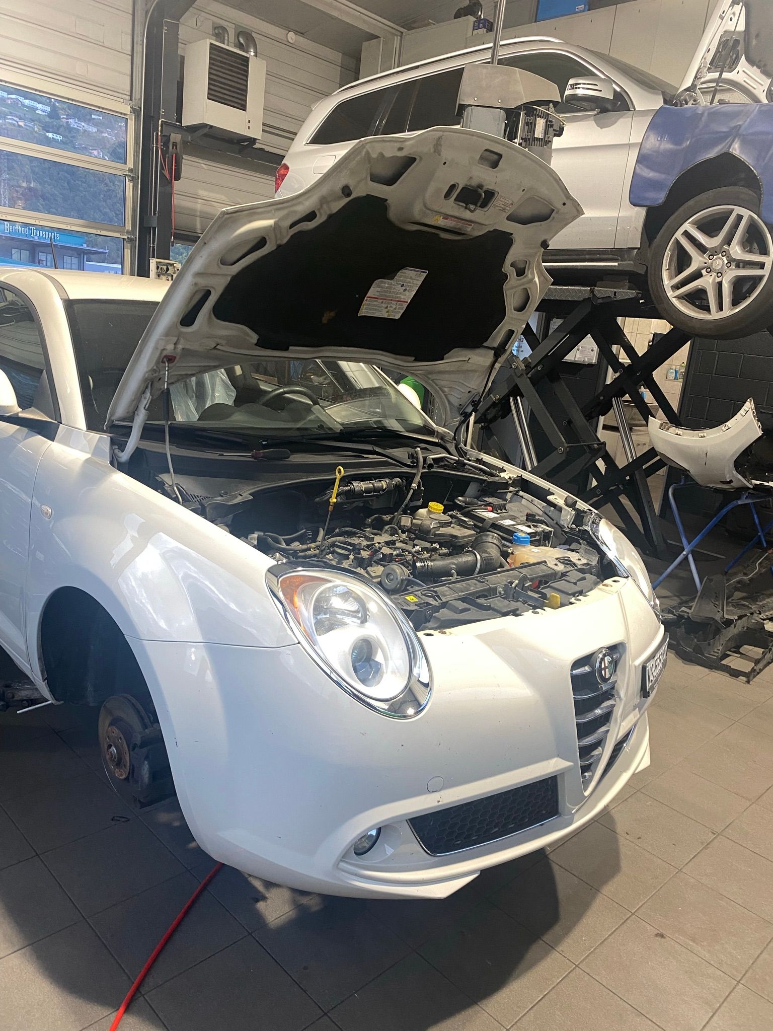 Une voiture blanche avec le capot ouvert dans un garage.