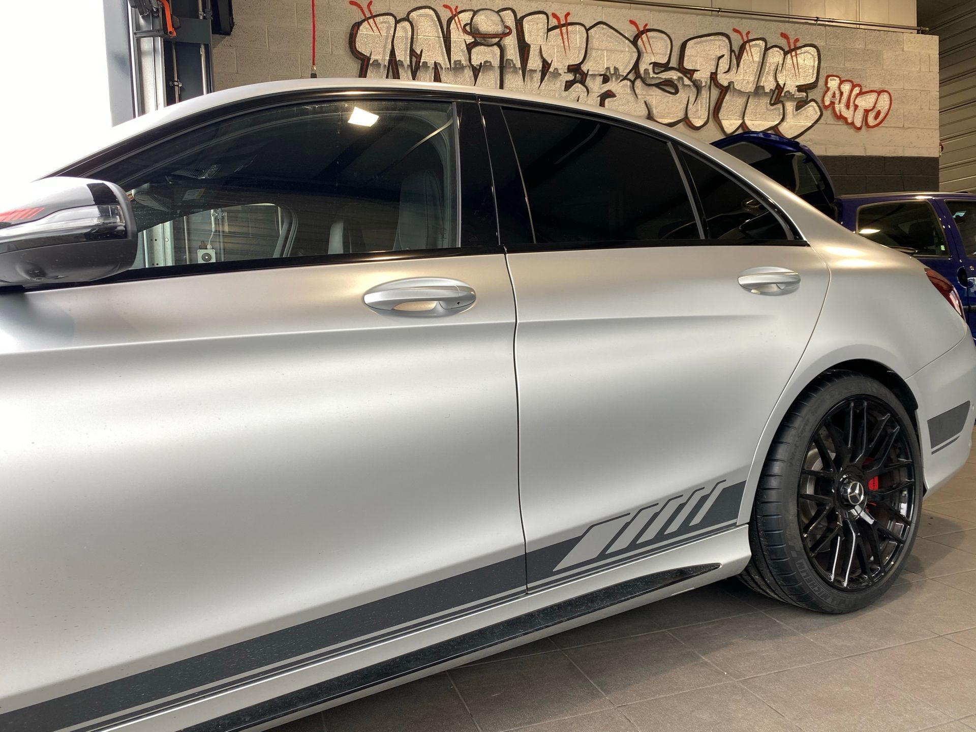 Une voiture argentée est garée dans un garage avec des graffitis sur le mur derrière elle.