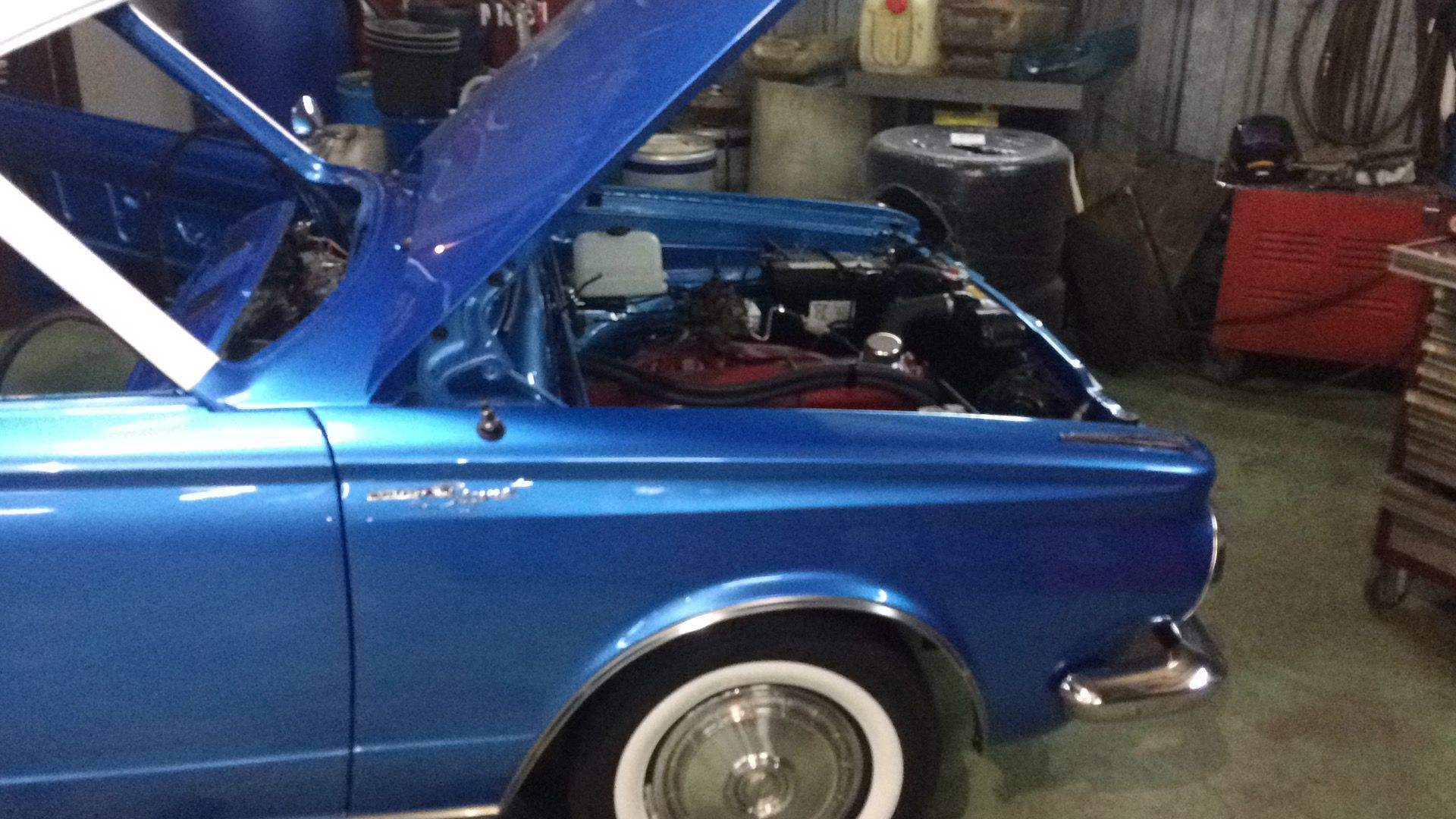 Une voiture bleue avec le capot ouvert se trouve dans un garage.