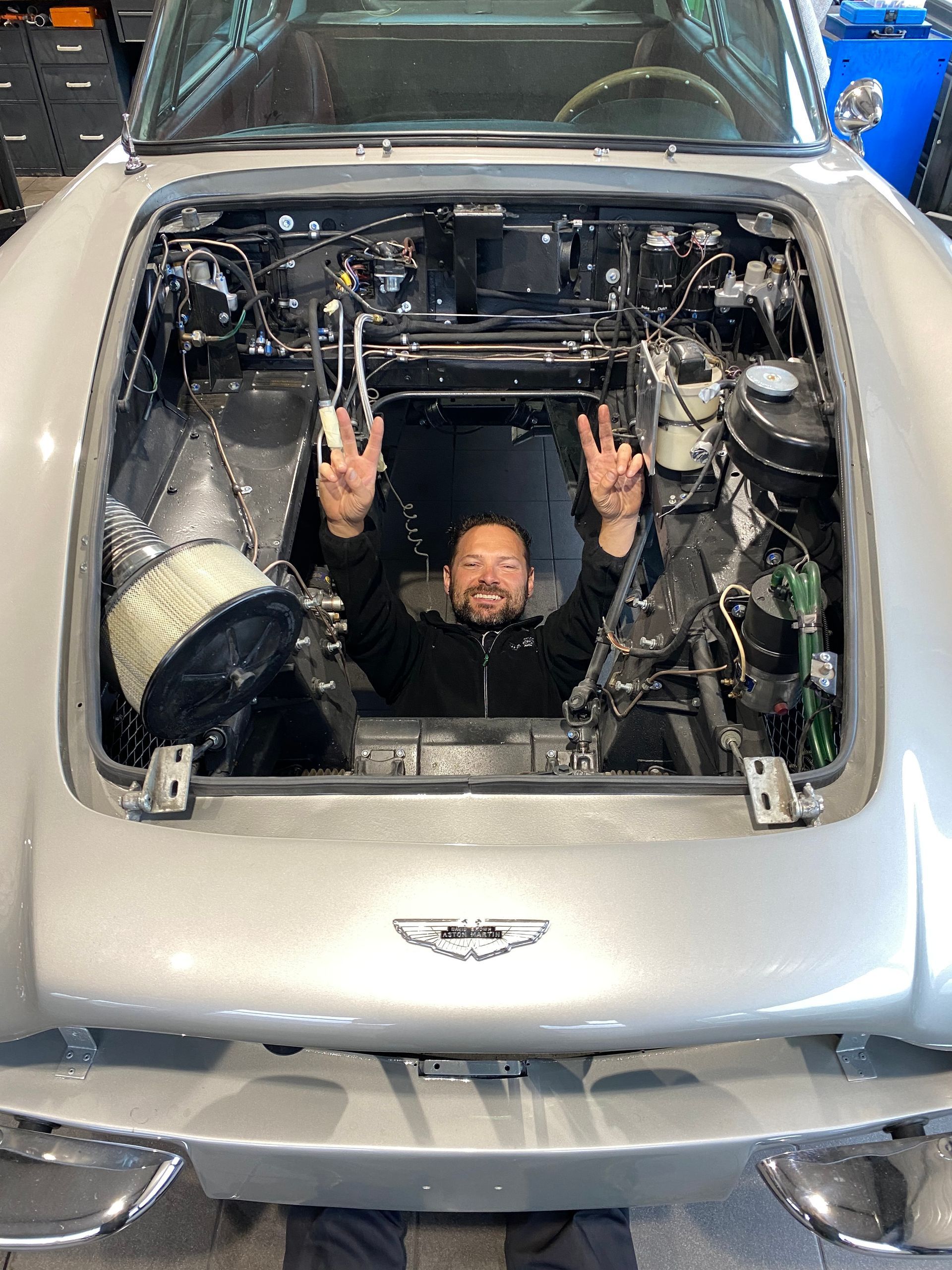 Un homme est assis sous le capot d’une voiture.