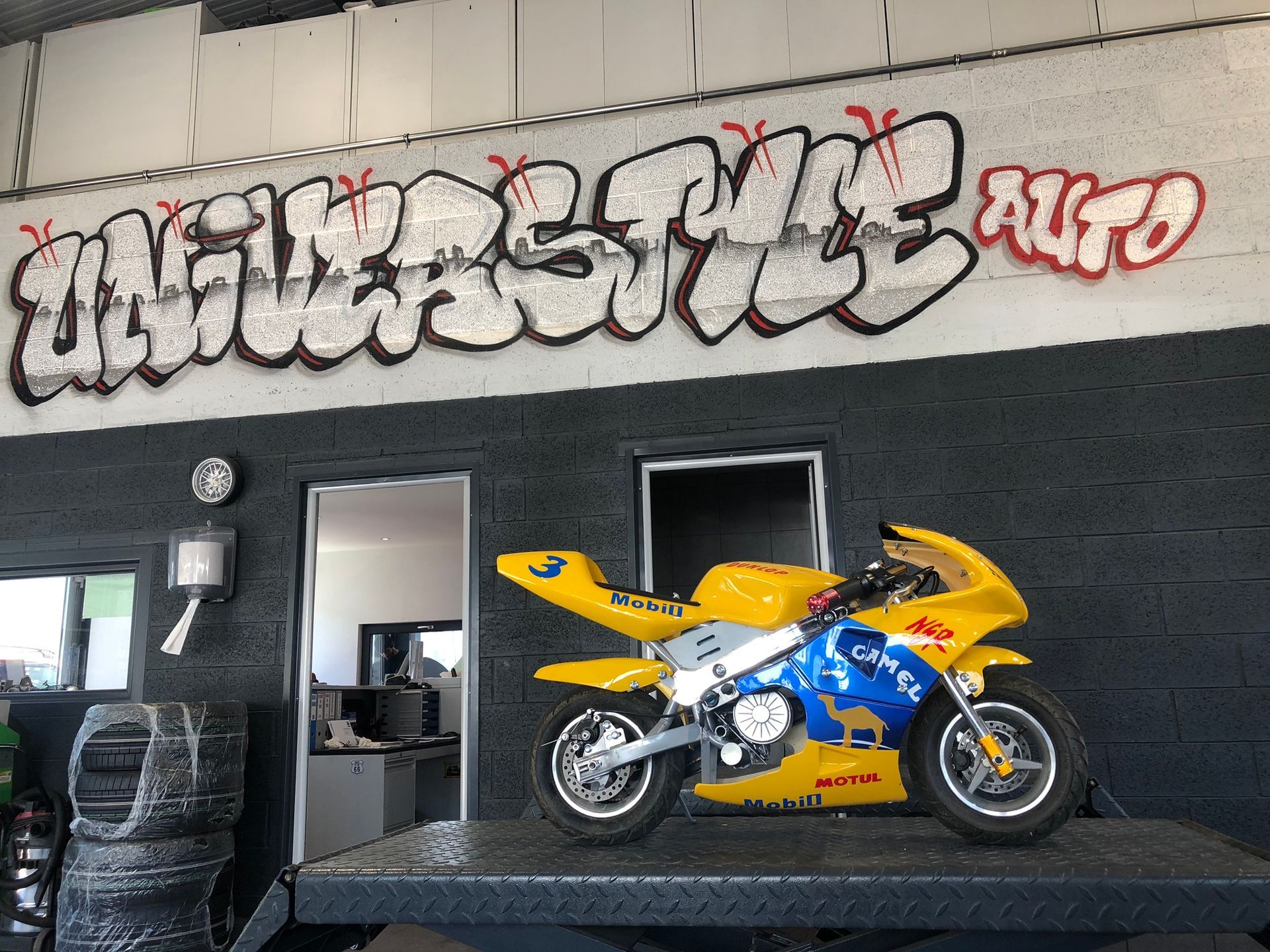 Une moto jaune et bleue est garée devant un mur couvert de graffitis.