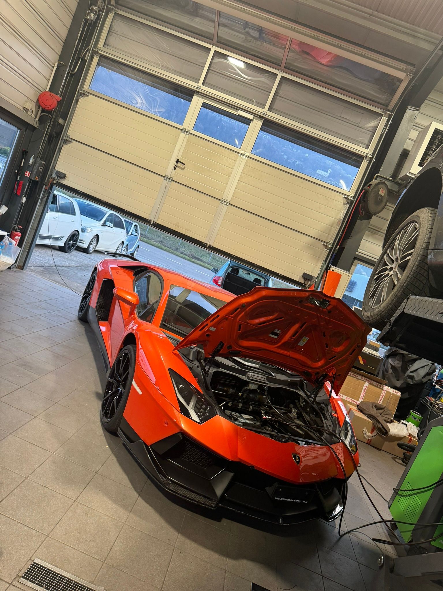 Une Lamborghini Aventador orange est garée dans un garage avec le capot ouvert.