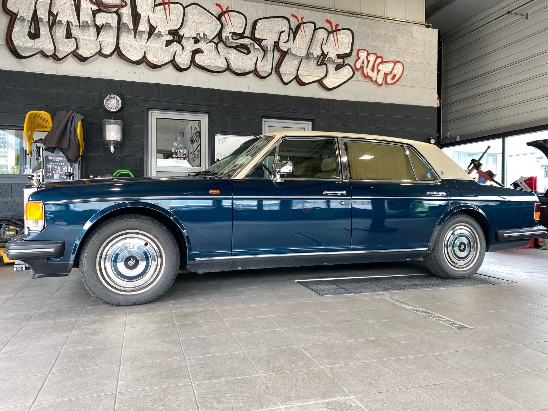Une voiture bleue est garée dans un garage avec des graffitis sur le mur.