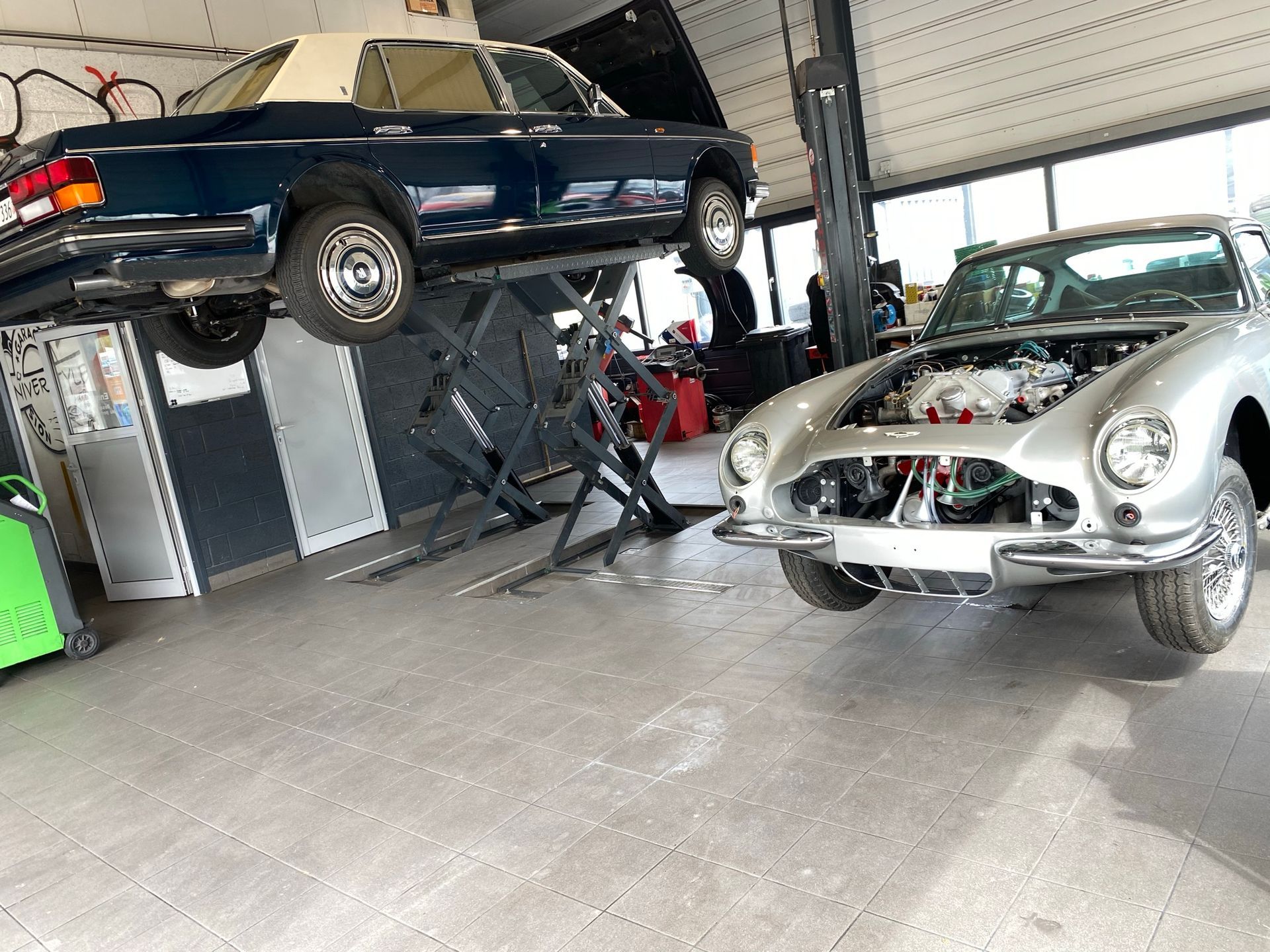 Deux voitures sont posées sur un ascenseur dans un garage.